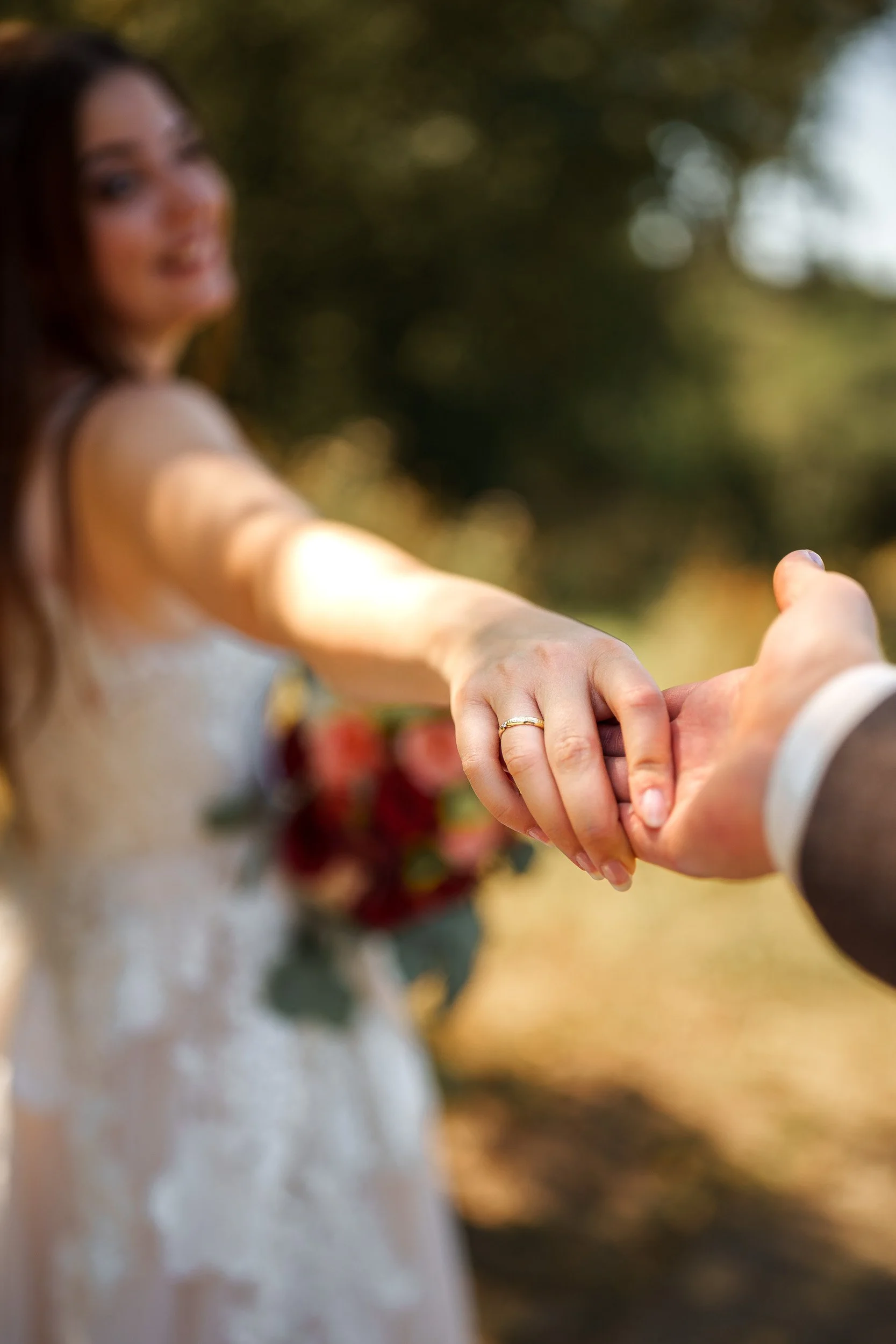 Nahaufnahme eines Paares beim Händeschütteln, im Hintergrund ist eine Frau im Brautkleid mit Blumenstrauß sichtbar.