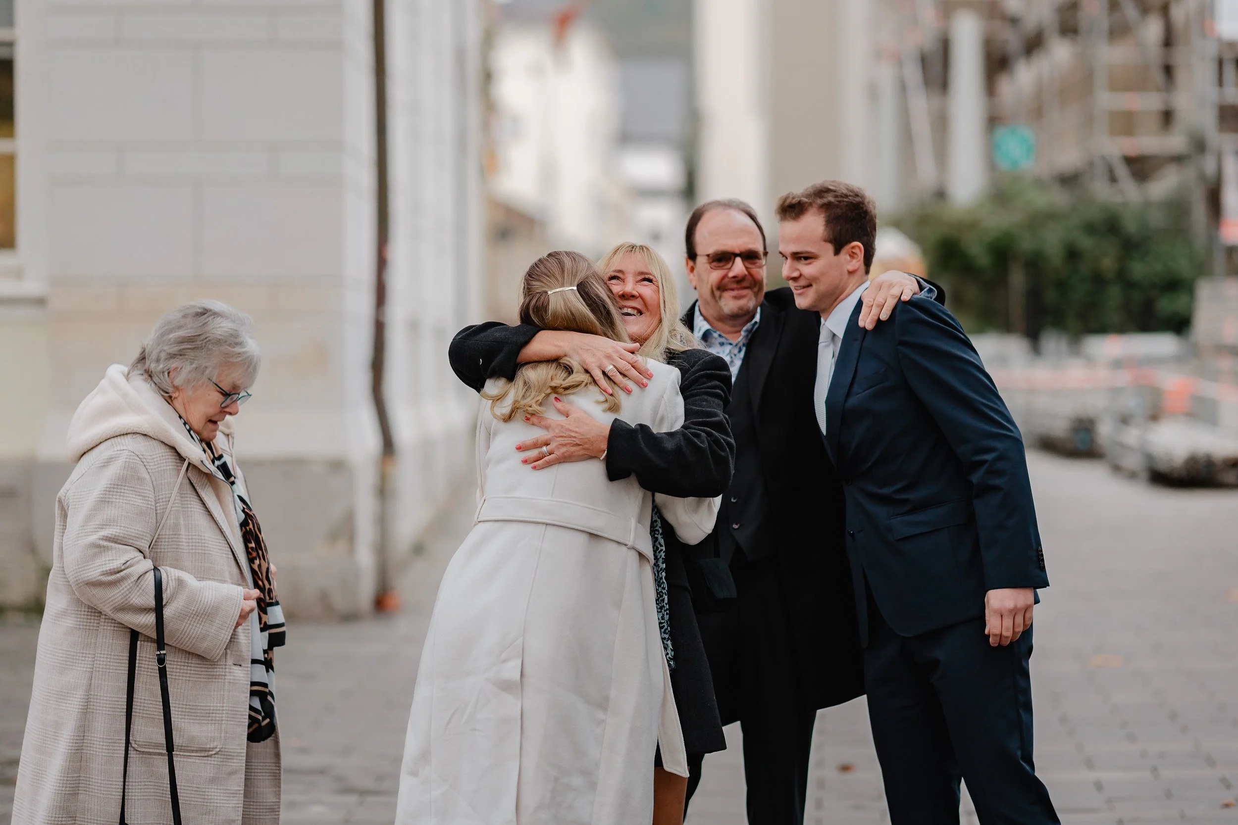 Gruppe von Menschen, die sich auf einer Straße umarmen und freuen, während im Hintergrund Bauarbeiten und Gebäude sichtbar sind.