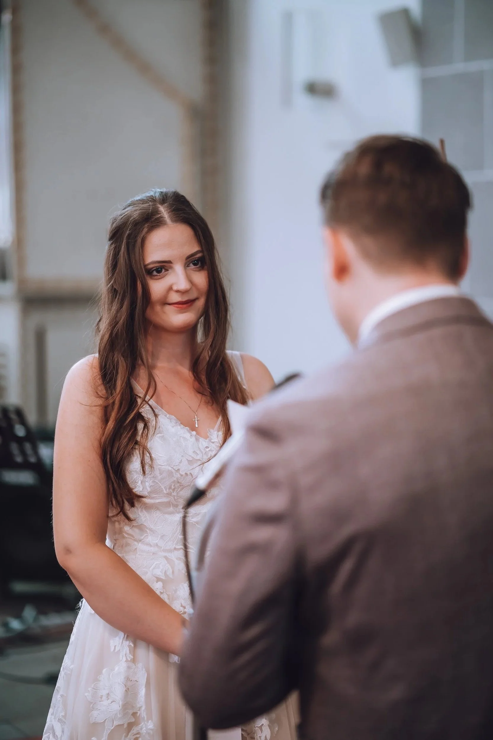 Ein Mädchen in weißem Brautkleid bei einer standesamtlichen Trauung, es schaut den Mann an, der vor ihr steht.