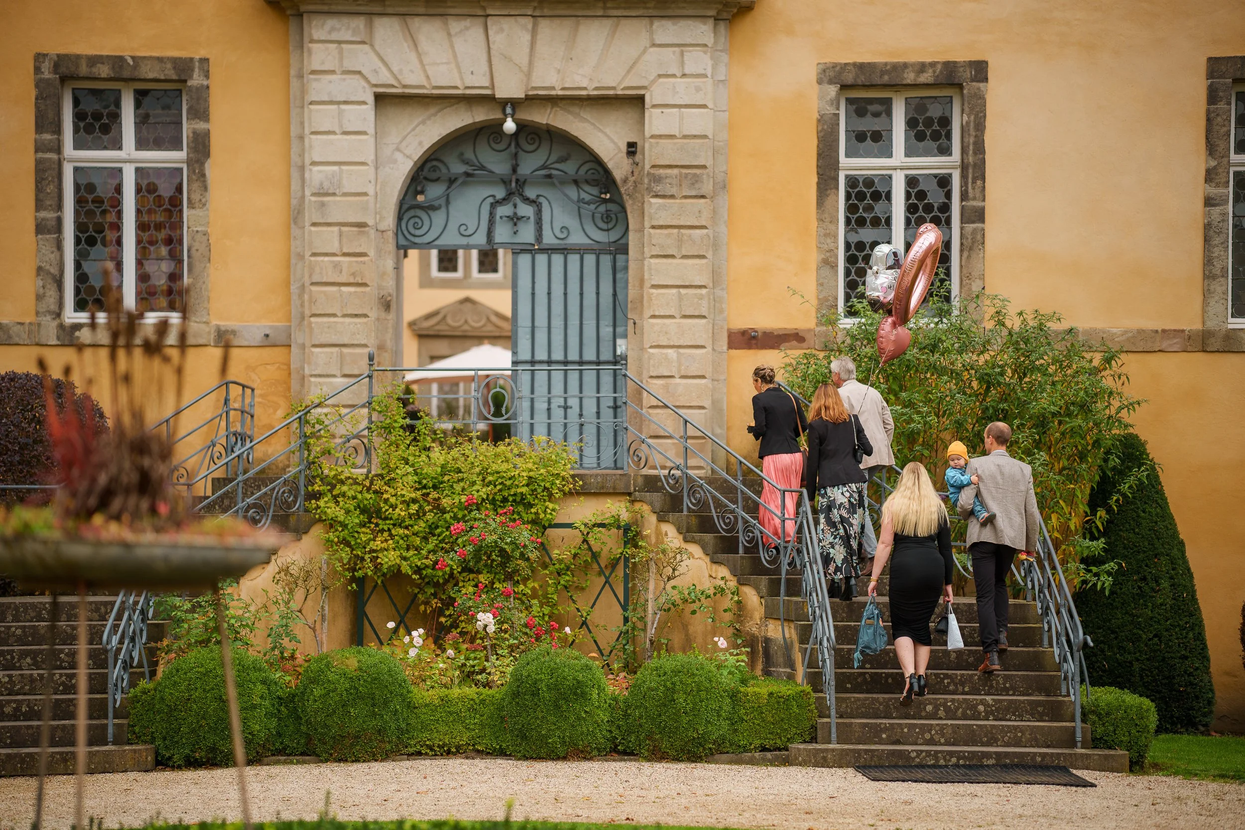 Familie steigt die Treppe zu einem gelben Gebäude mit Steinrahmen um die Fenster und Tür.