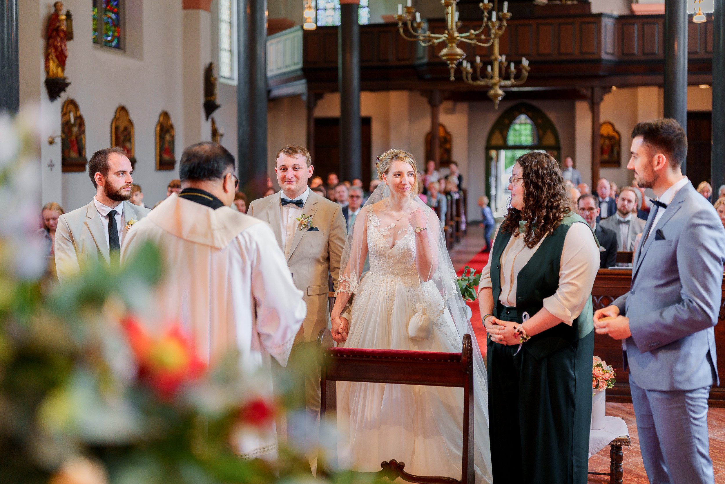 Eine Hochzeit in einer Kirche mit Braut, Bräutigam und Trauzeugen, umgeben von Gästen.