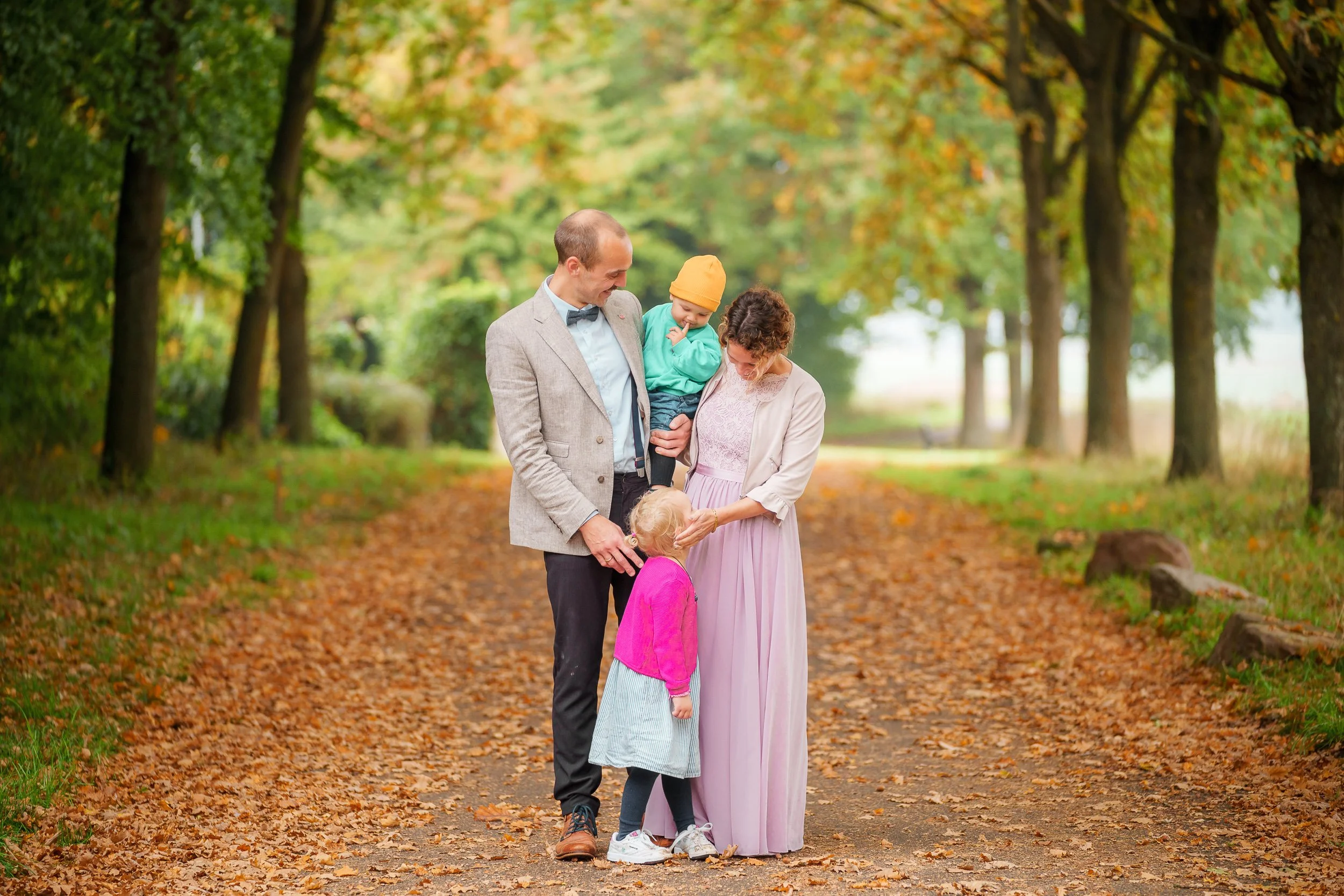 Familie mit zwei Kindern steht fröhlich auf einem herbstlichen Waldweg.