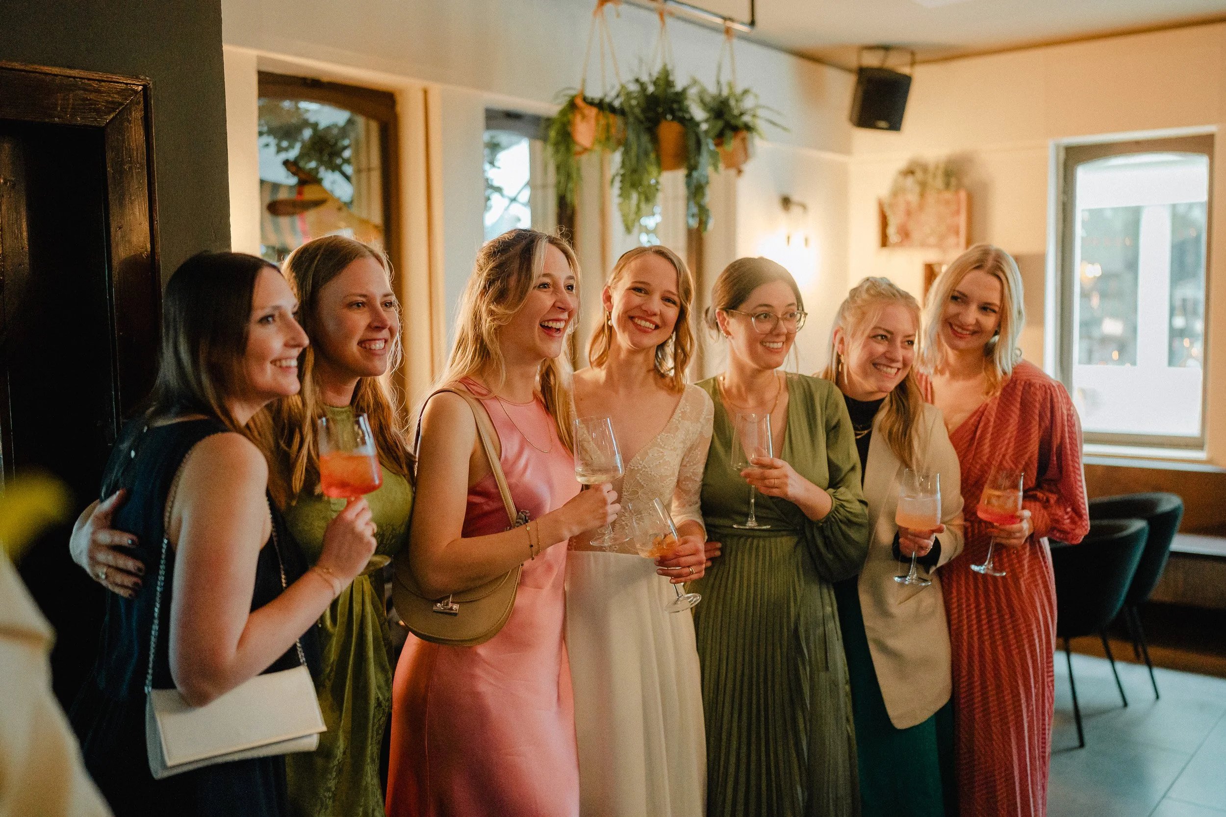 Eine Gruppe weiblicher Freunde bei einer Feier, die zusammen stehen, lachen und Getränke in einem gemütlichen Raum halten.