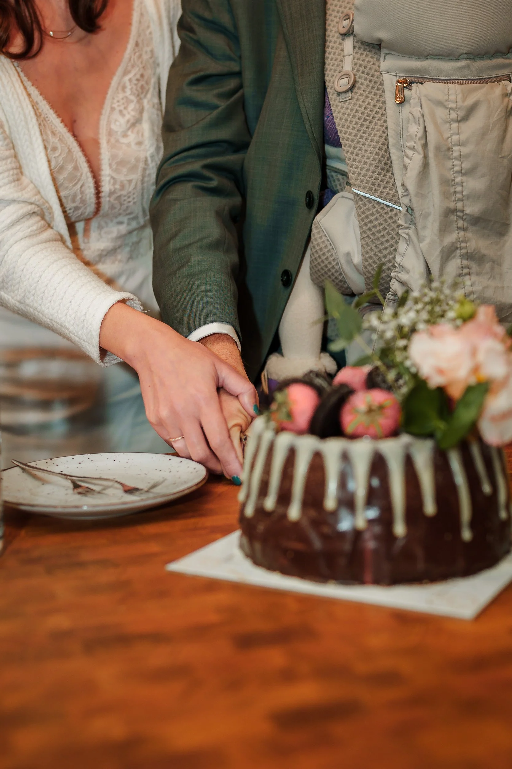 Ein Paar schneidet eine Hochzeitstorte mit Schokoladeüberzug, weiße Schokoglasur und Erdbeeren, während sie Hand in Hand an einem Holzschnittpunkt stehen.
