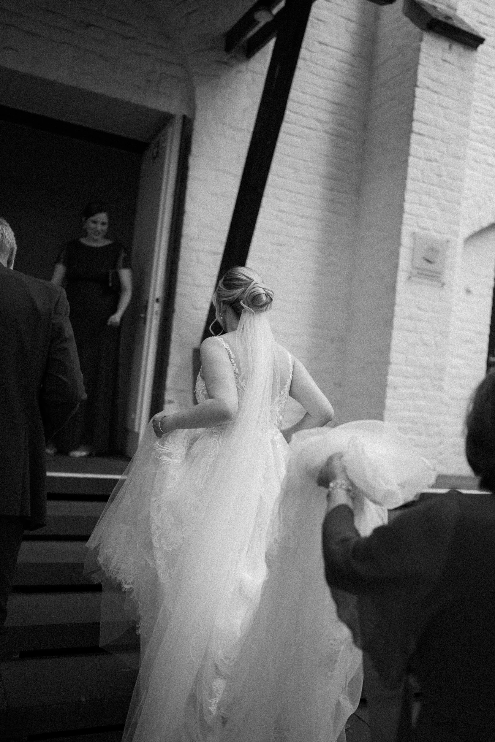 Braut steigt die Treppe im Kirchenraum hinauf, während Gäste sie begleiten, in Schwarz-Weiß-Fotografie.