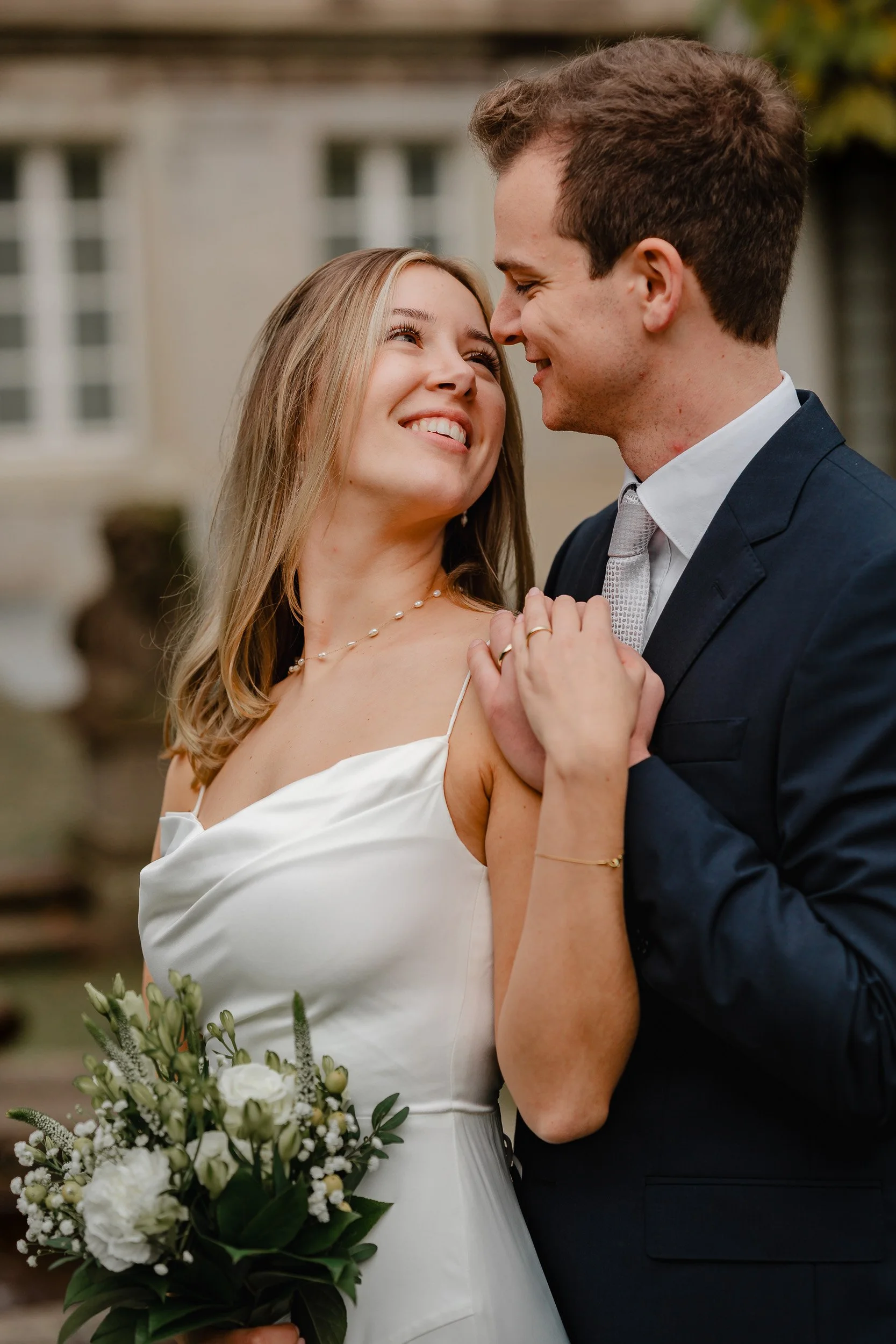Ein verliebtes Paar bei einer Hochzeit, die Frau hält einen Blumenstrauß, sie lächeln sich liebevoll an.