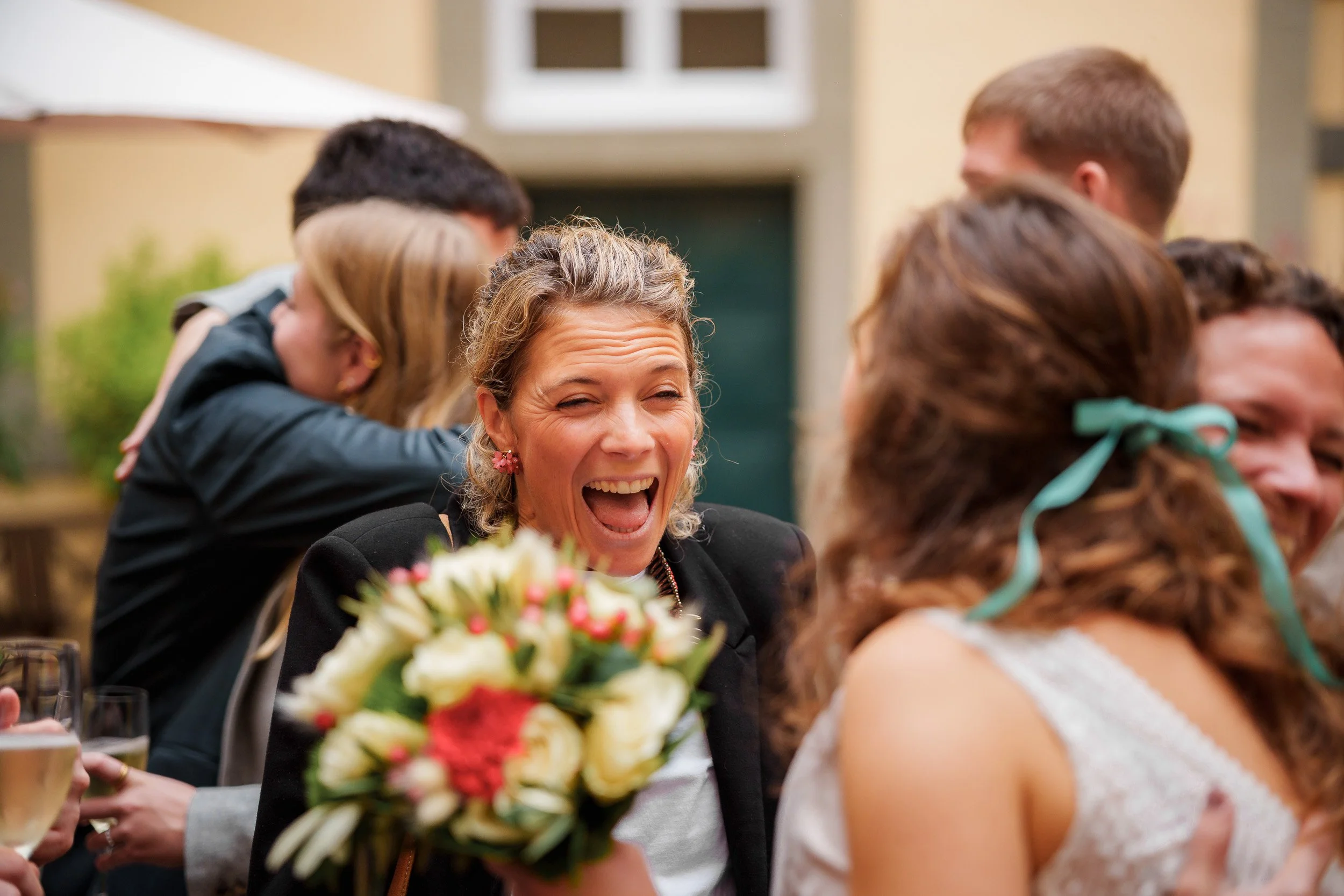 Menschen feiern draußen, eine Frau mit Blumenstrauß lacht fröhlich.