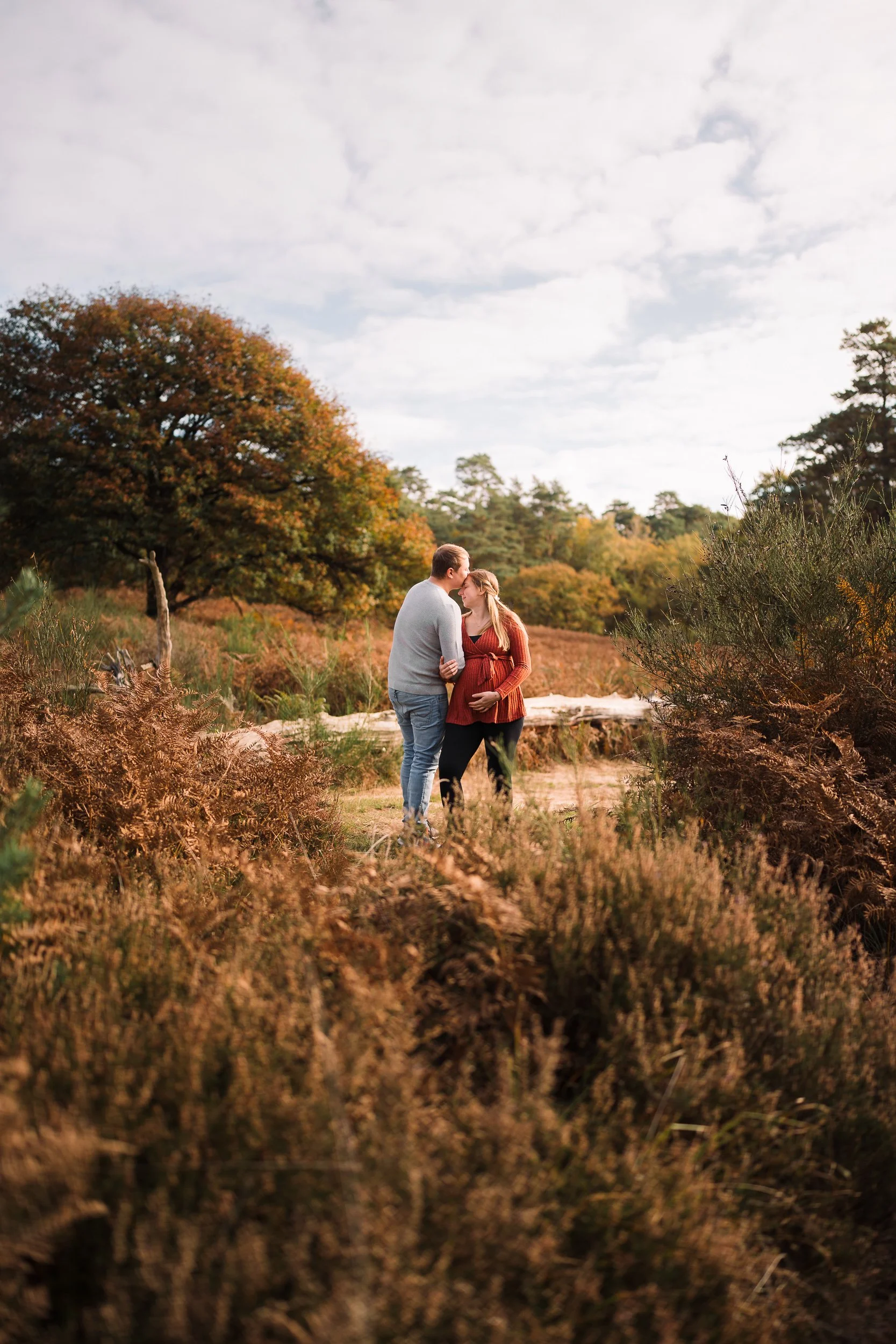 Ein Paar, das sich bei Sonnenuntergang in einer Naturkulisse küsst, umgeben von Büschen und Bäumen, mit einem Weg im Vordergrund.