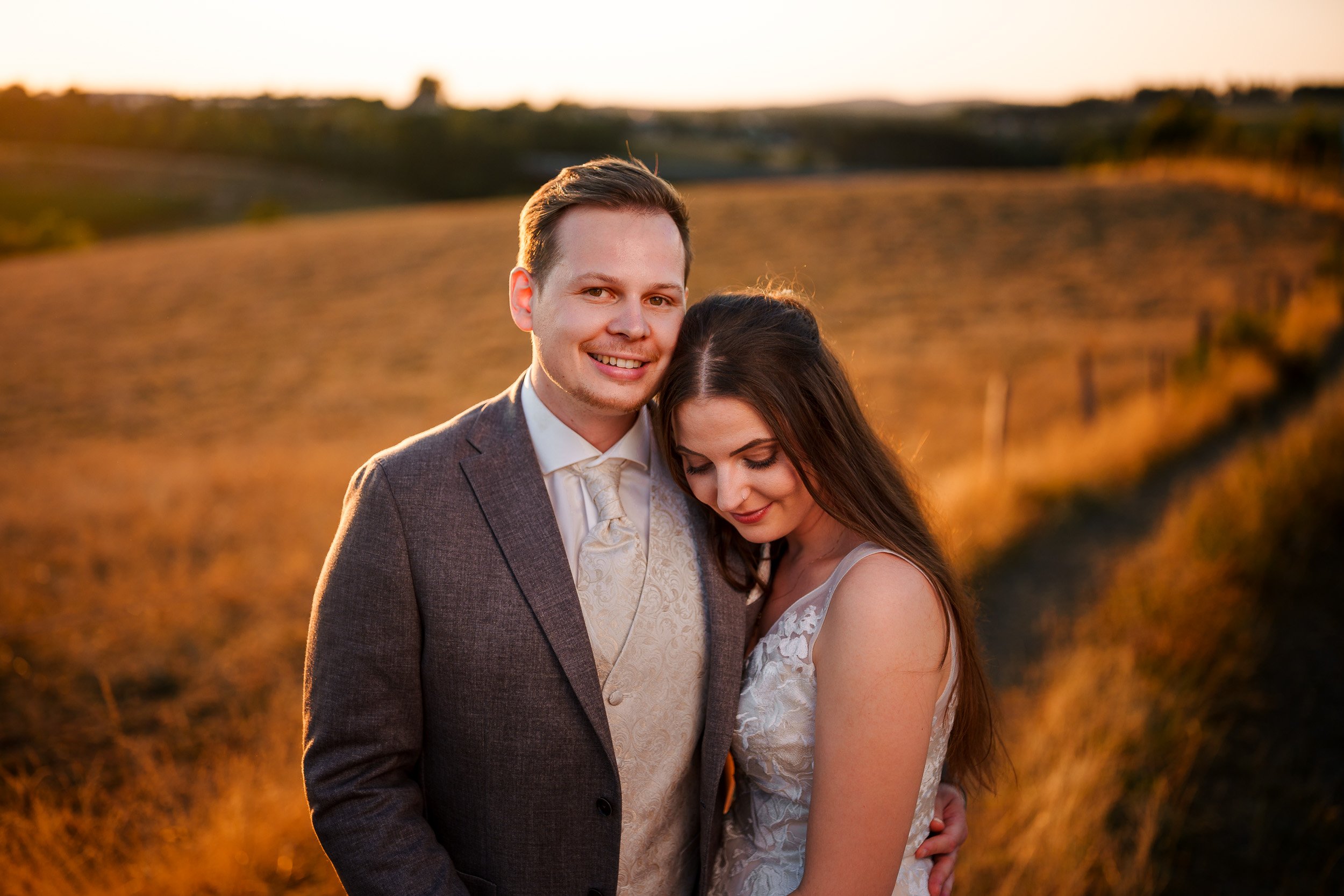 Ein verliebtes Paar in formeller Kleidung umarmt sich im Sonnenuntergang in einer ländlichen Umgebung.