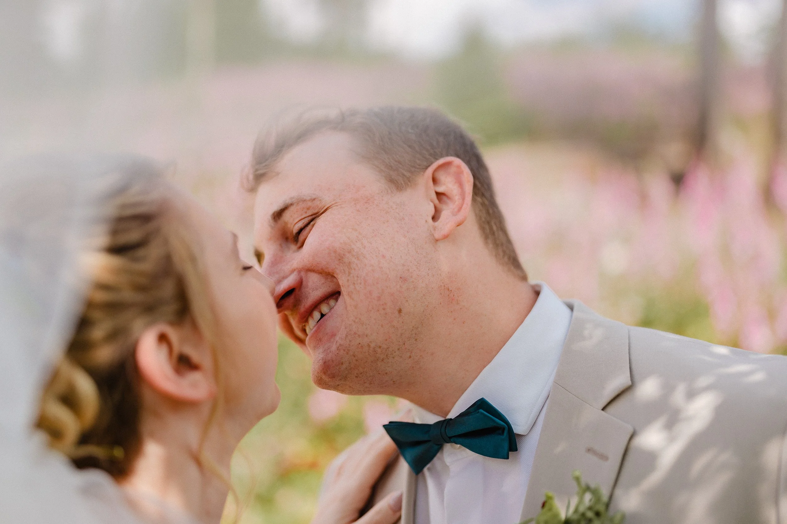 Ein Brautpaar bei einer Hochzeit, das sich anlächelt, mit einem blühenden Garten im Hintergrund.