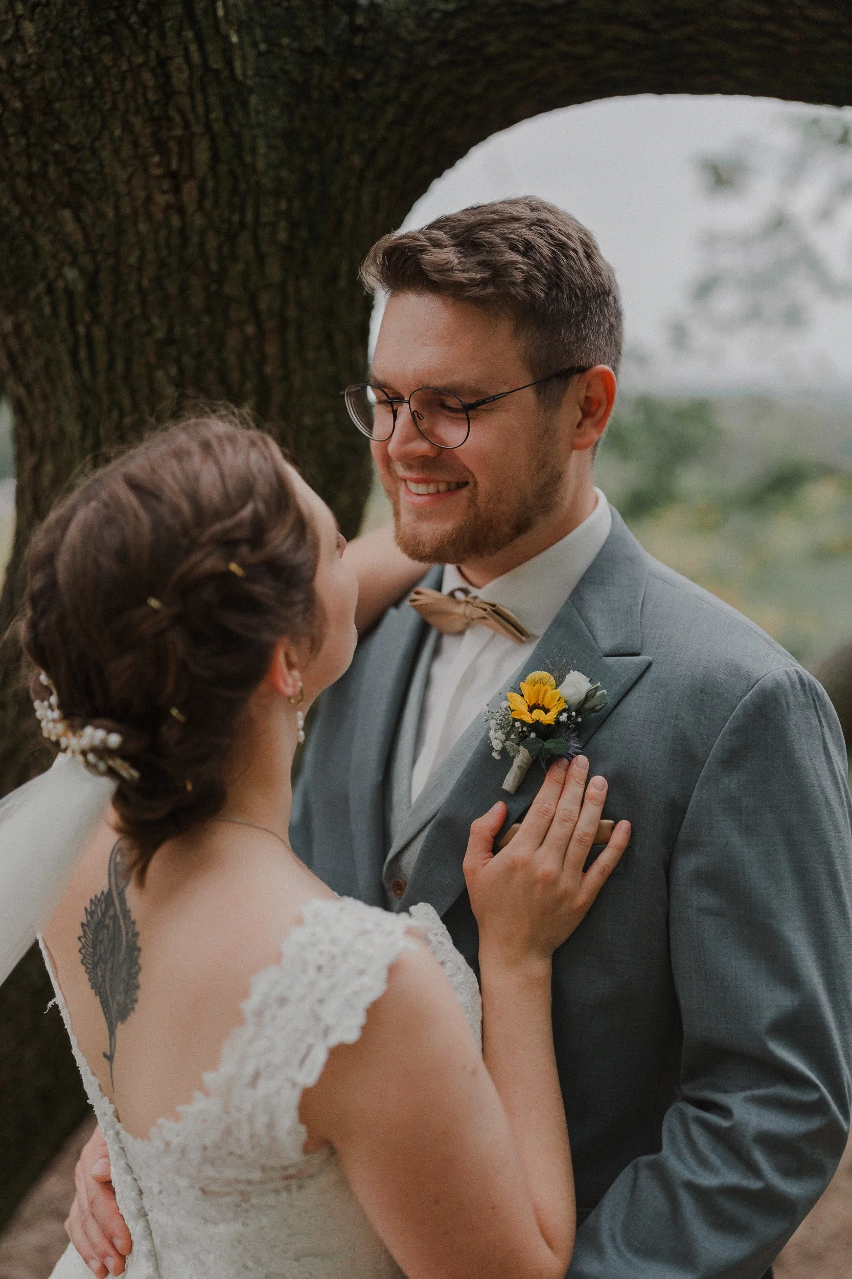 Braut und Bräutigam stehen sich nah vor einem Baum und lächeln sich an.