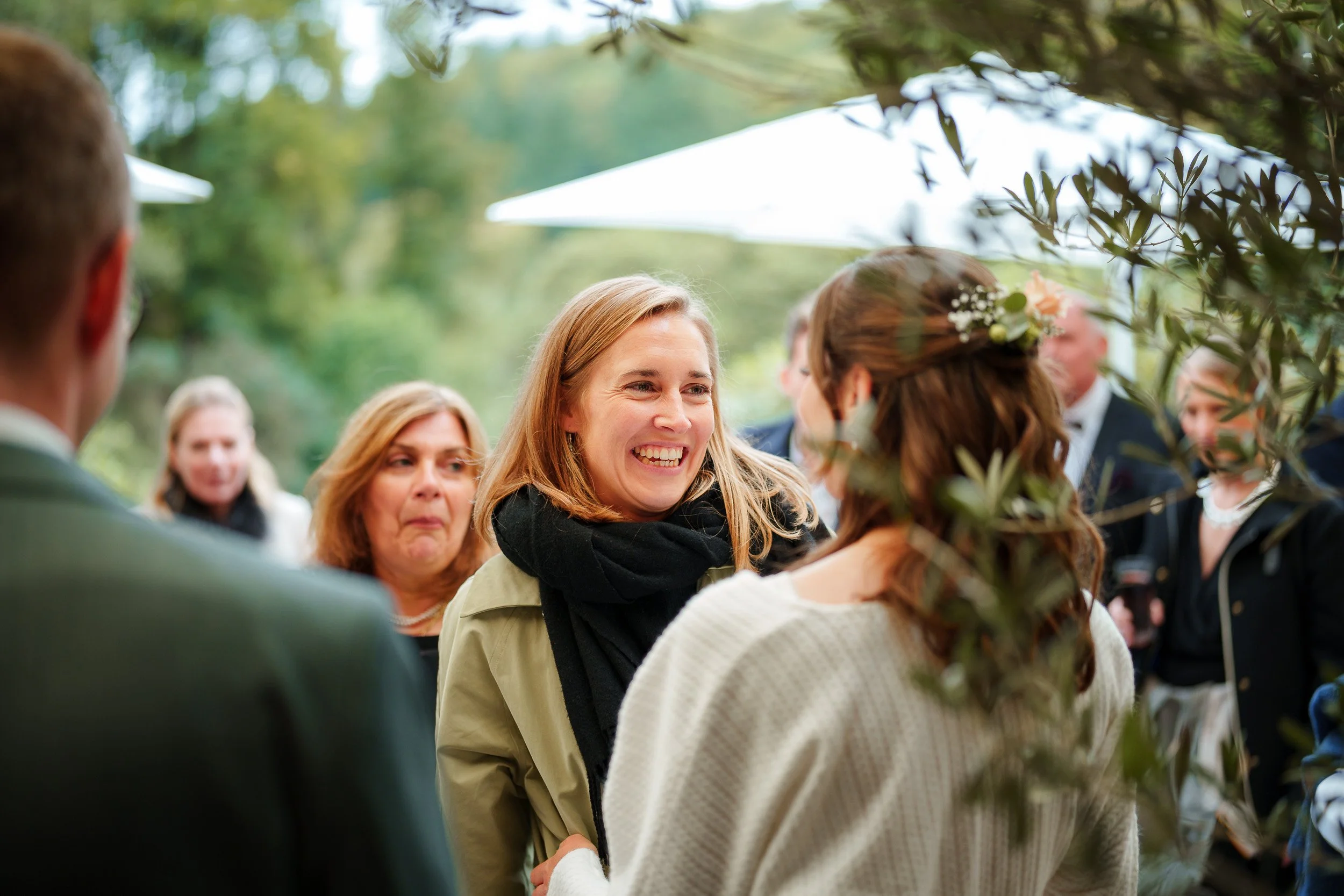 Menschen bei einer Gartenhochzeit, Frau in weißen Kleid mit Blümchen im Haar, freundliches Gespräch im Freien