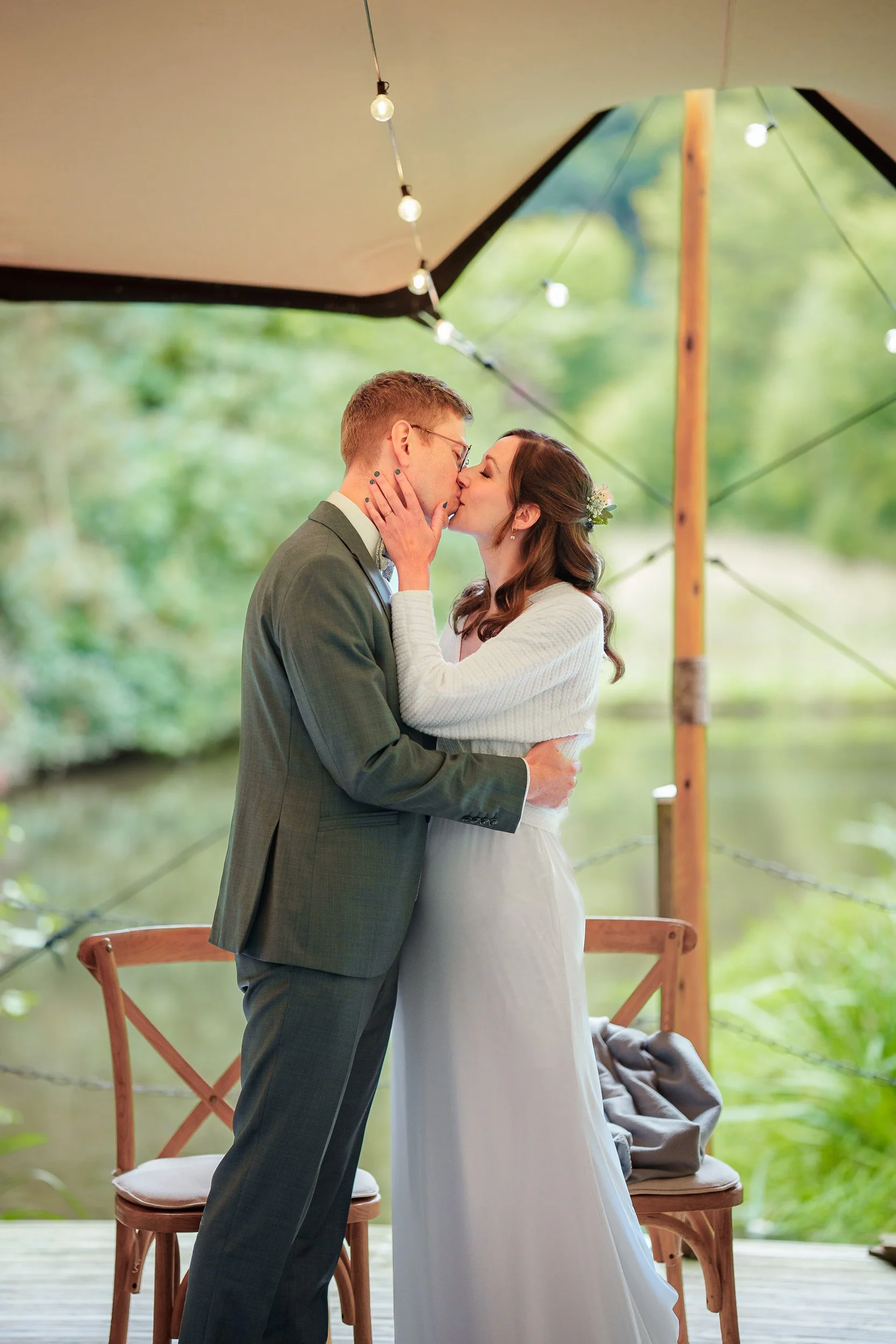 Ein Brautpaar küsst sich unter einem Pavillon mit Lichterketten bei einer Hochzeit im Freien.