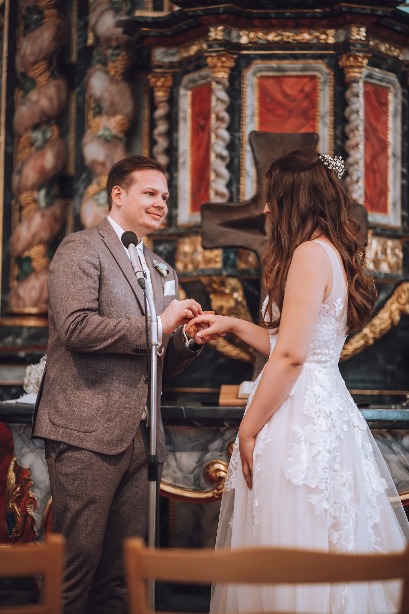 Ein Brautpaar bei der Trauung in einer Kirche, der Bräutigam steckt den Ehering an die Hand der Braut.