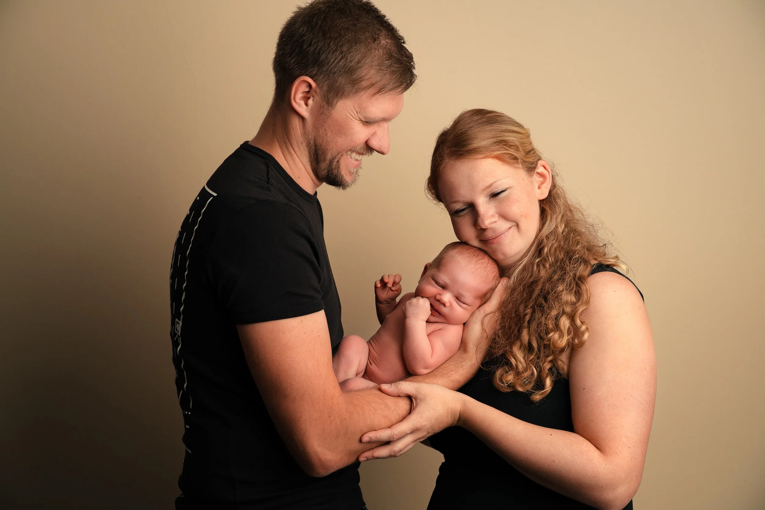 Ein glückliches Paar hält ein neugeborenes Baby und schaut liebevoll auf das Kind.