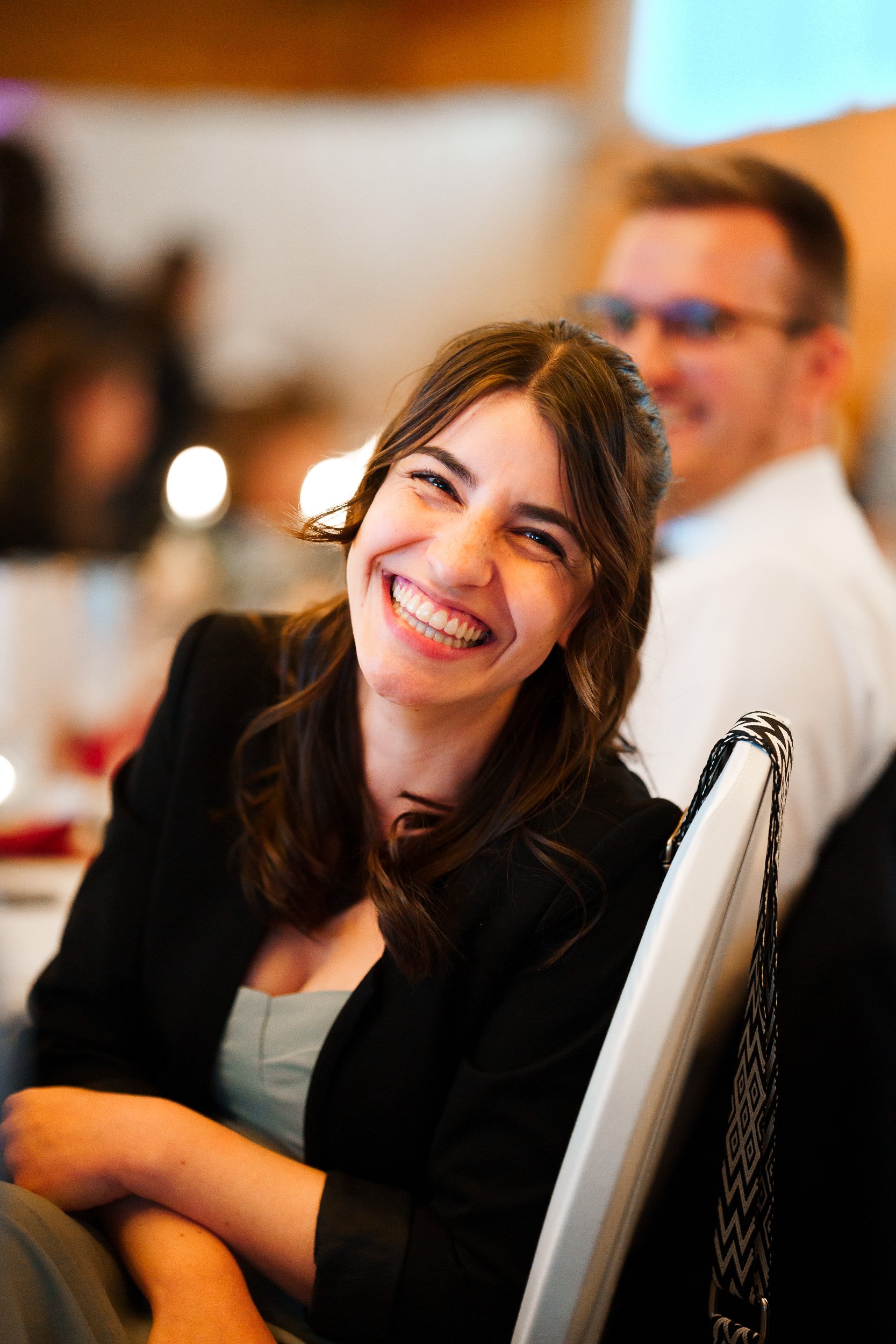 Lächelnde Frau bei einer Veranstaltung, im Hintergrund ein lächelnder Mann.