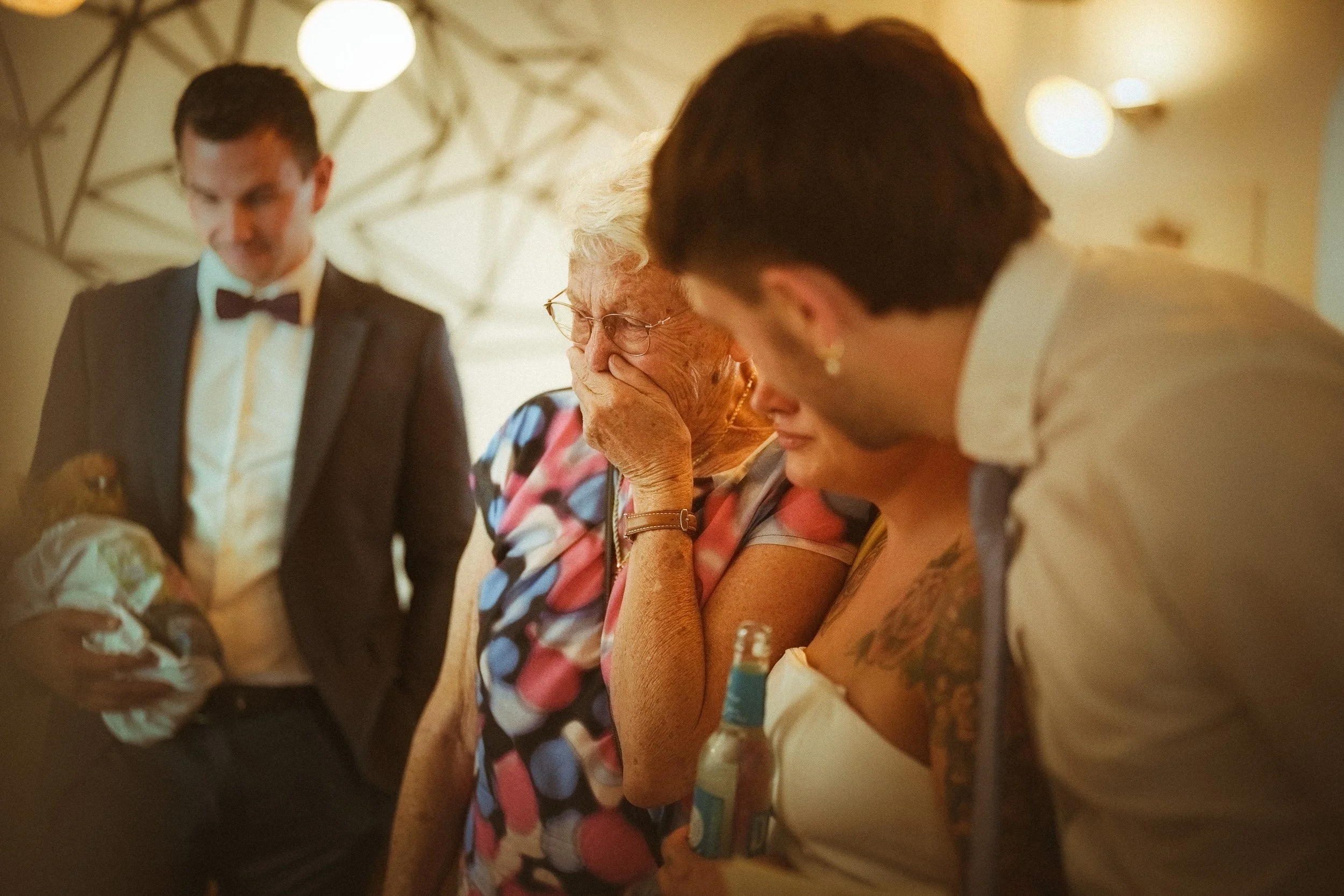 Eine Gruppe von Menschen bei einer Feier, im Vordergrund eine ältere Frau, die weint. Neben ihr zwei Frauen und zwei Männer, die anhören oder beobachten, was passiert.