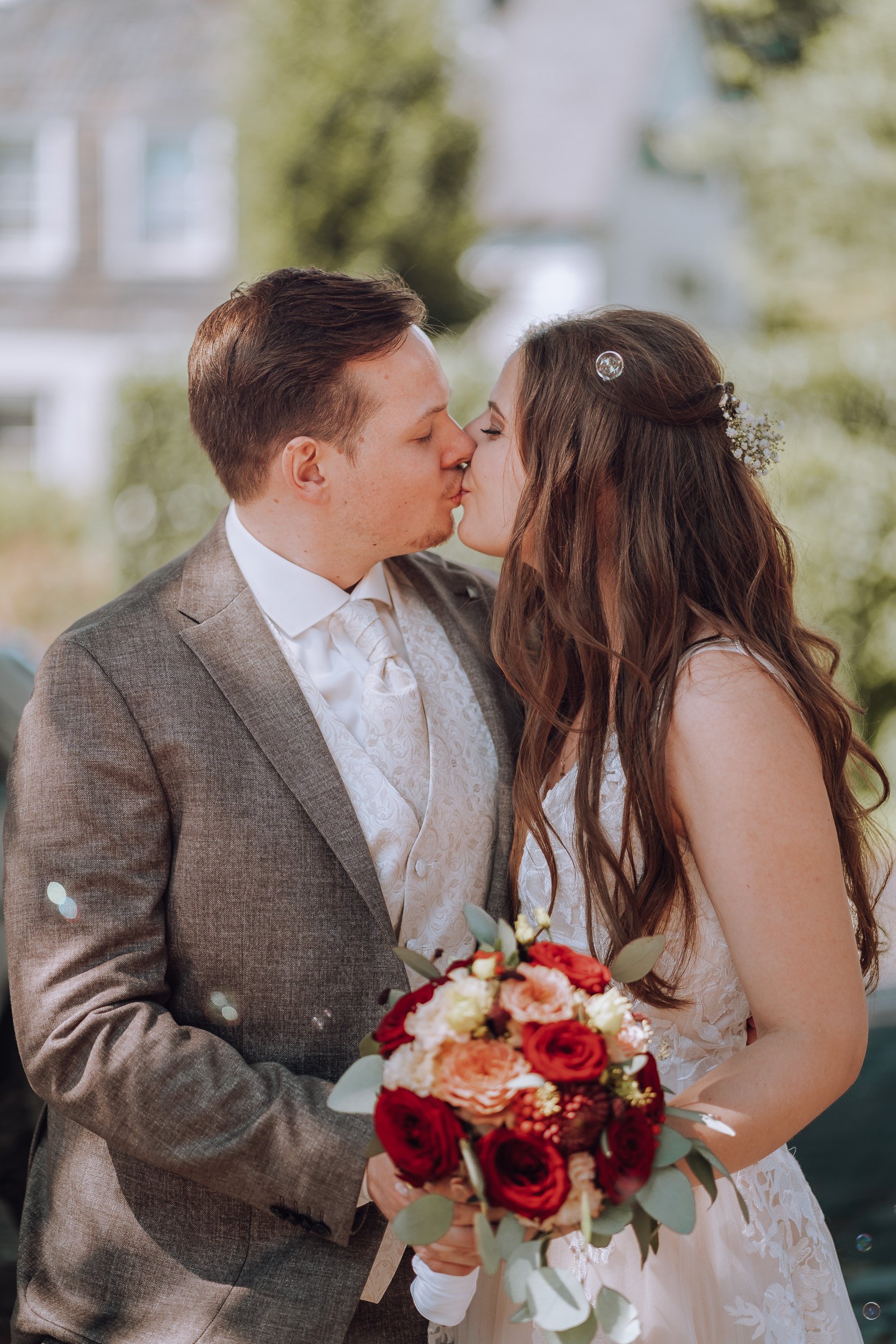 Ein frisch vermähltes Paar beim Kuss, die Braut hält einen Blumenstrauß aus roten und weißen Rosen.