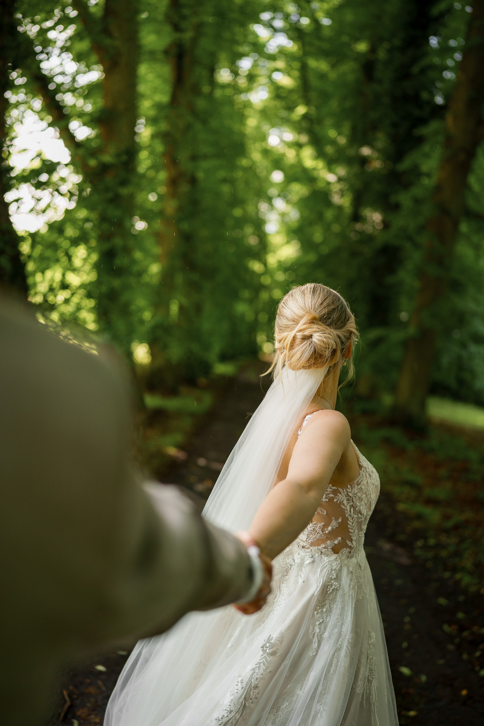 Braut in einem weißen Hochzeitskleid und Schleier, die durch einen Wald geht, während der Fotograf sie fotografiert.