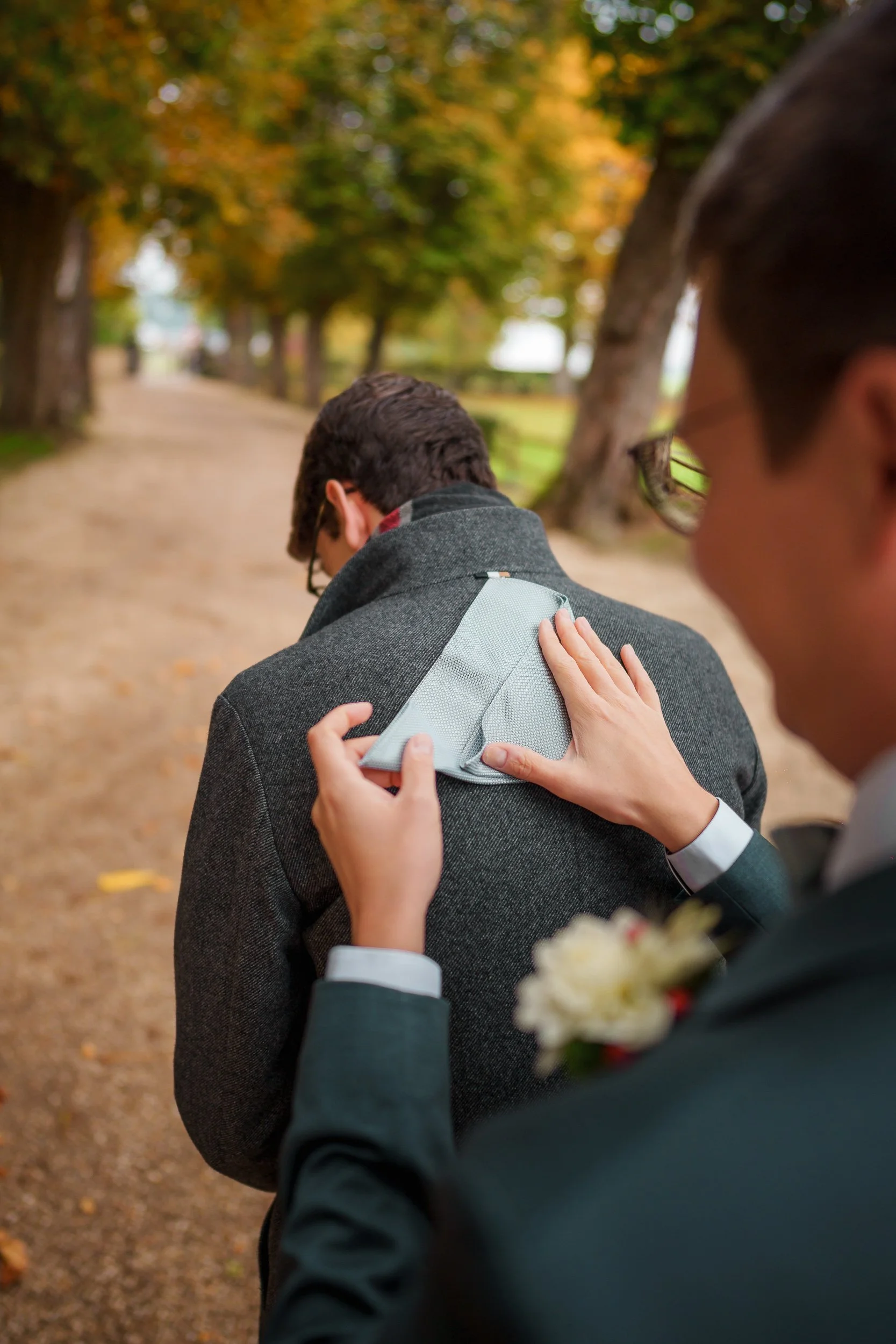 Ein Mann steckt einem anderen Mann im grauen Mantel in einem Park mit herbstlichen Bäumen eine gelbe Notiz.