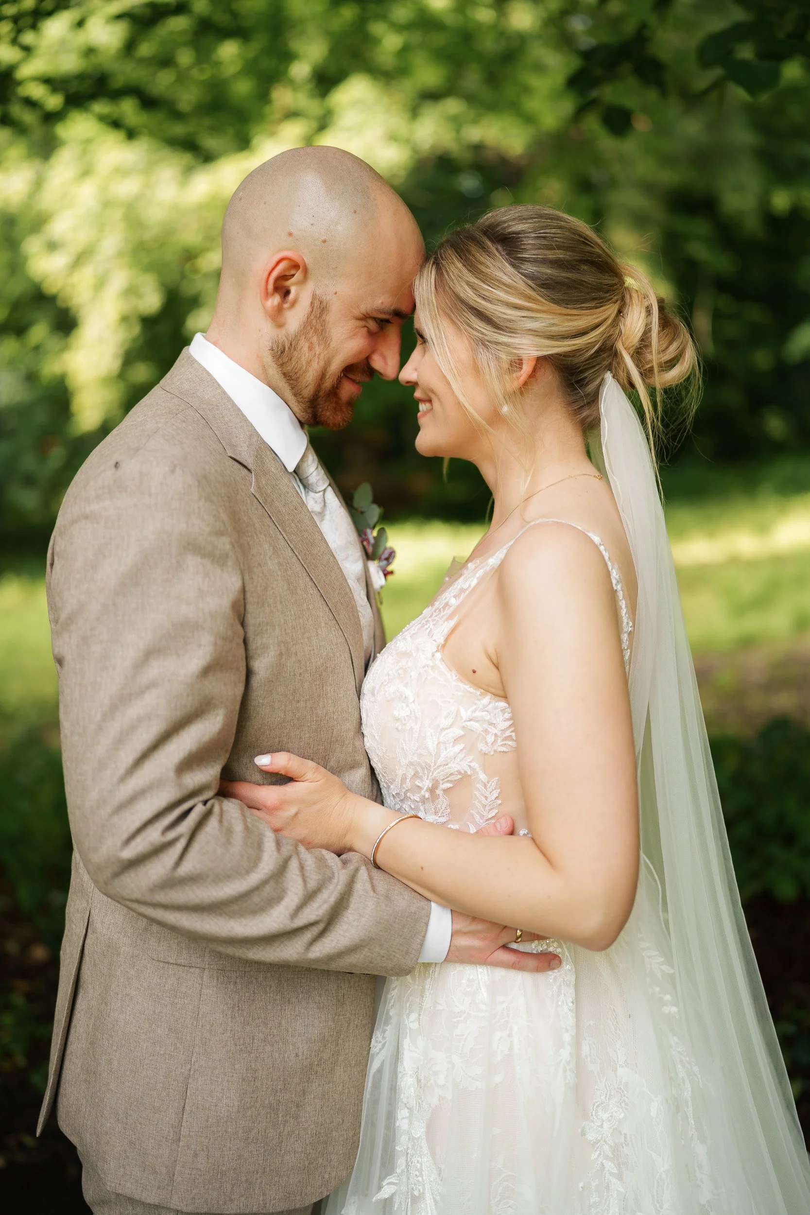Braut und Bräutigam stehen sich im Freien, ihre Stirn berühren sich, lächeln glücklich, bei ihrer Hochzeit.