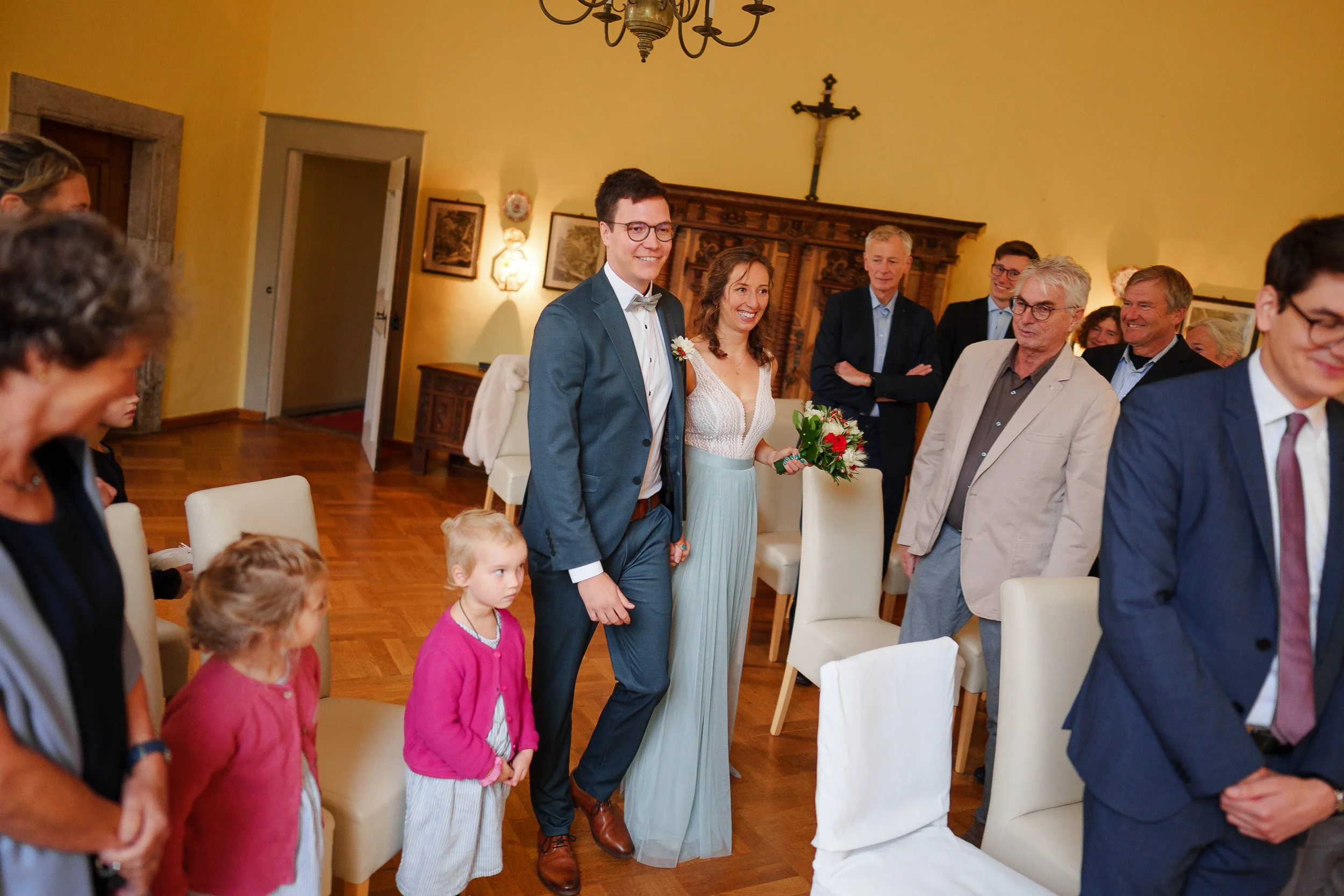 Hochzeitspaar bei der Trauung umgeben von Gästen in einem festlich dekorierten Raum.