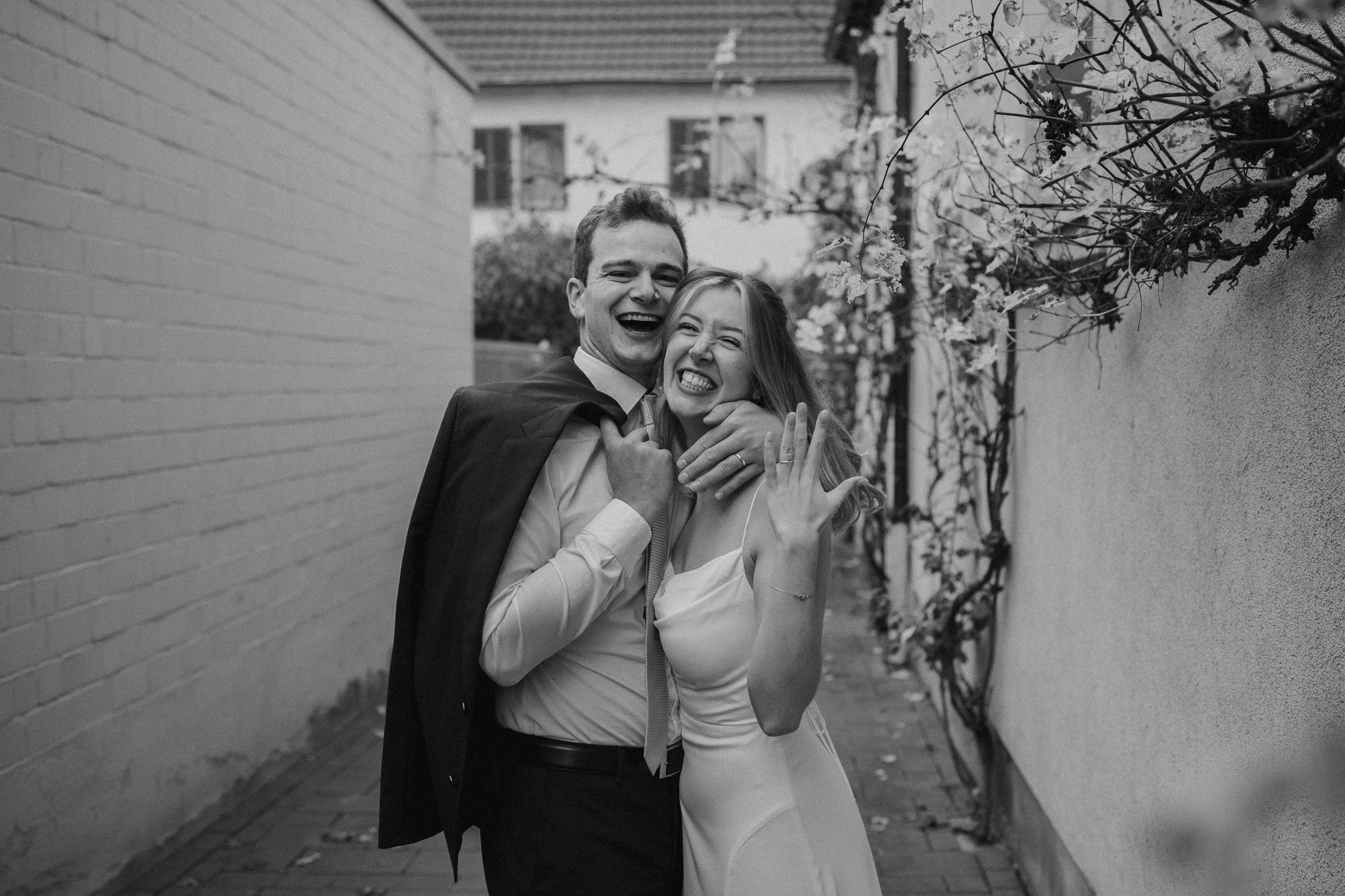 Ein glückliches Paar in formeller Kleidung, das in einer engen Gasse lacht und sich umarmt.
