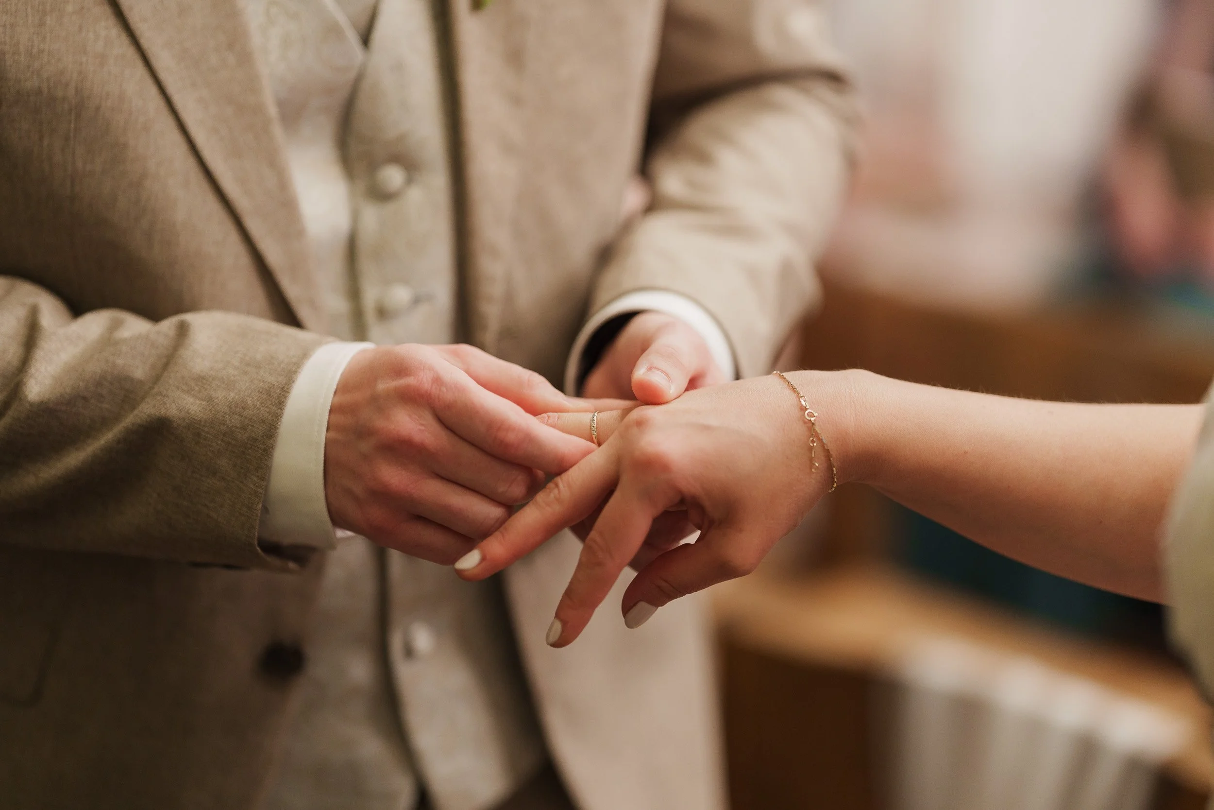 Ein Paar bei einer Heirat, wobei der Partner den Ehering am Finger der Partnerin anlegt.