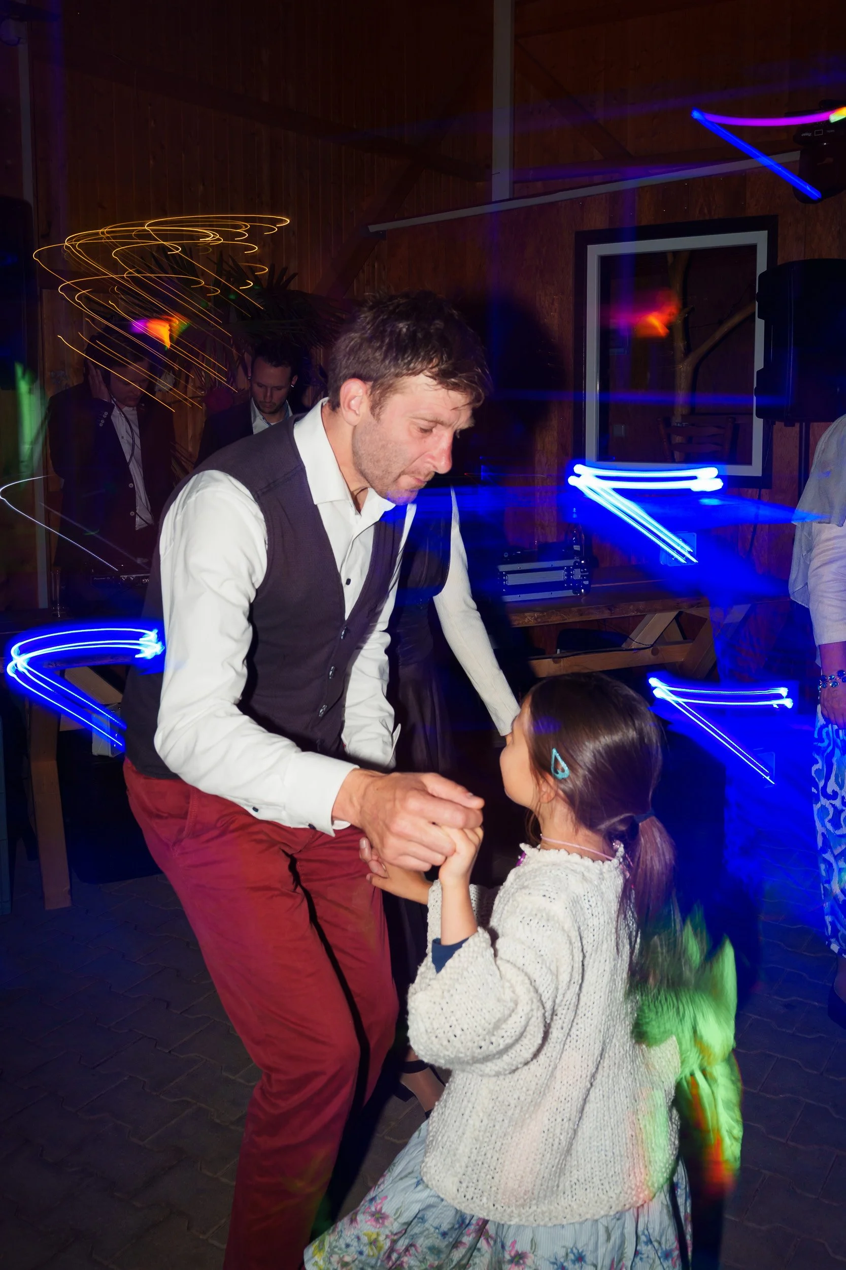 Ein Mann und ein Kind tanzen auf einer Party im dunklen Raum mit bunten Lichtstrahlen.