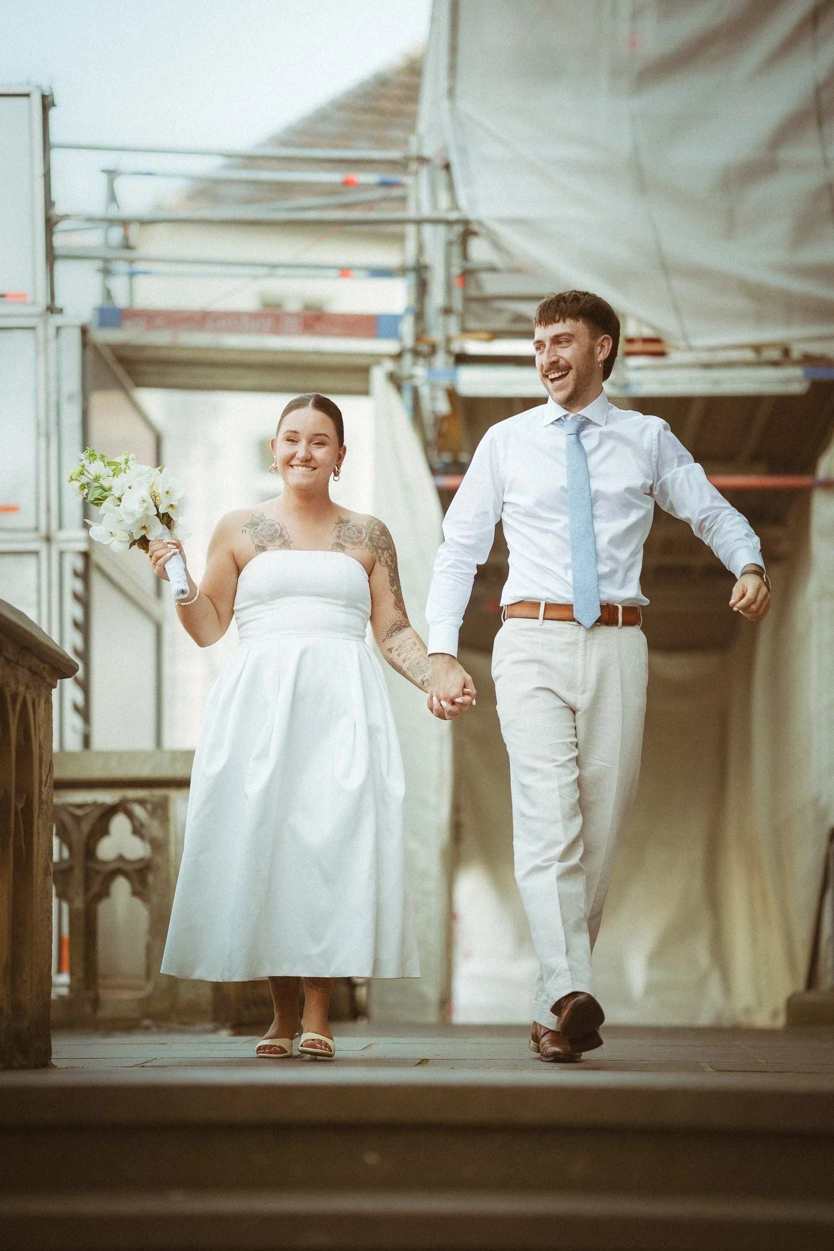Ein Brautpaar hält Händchen und geht lachend durch eine Baustelle, die für eine Hochzeitsfeier dekoriert ist.