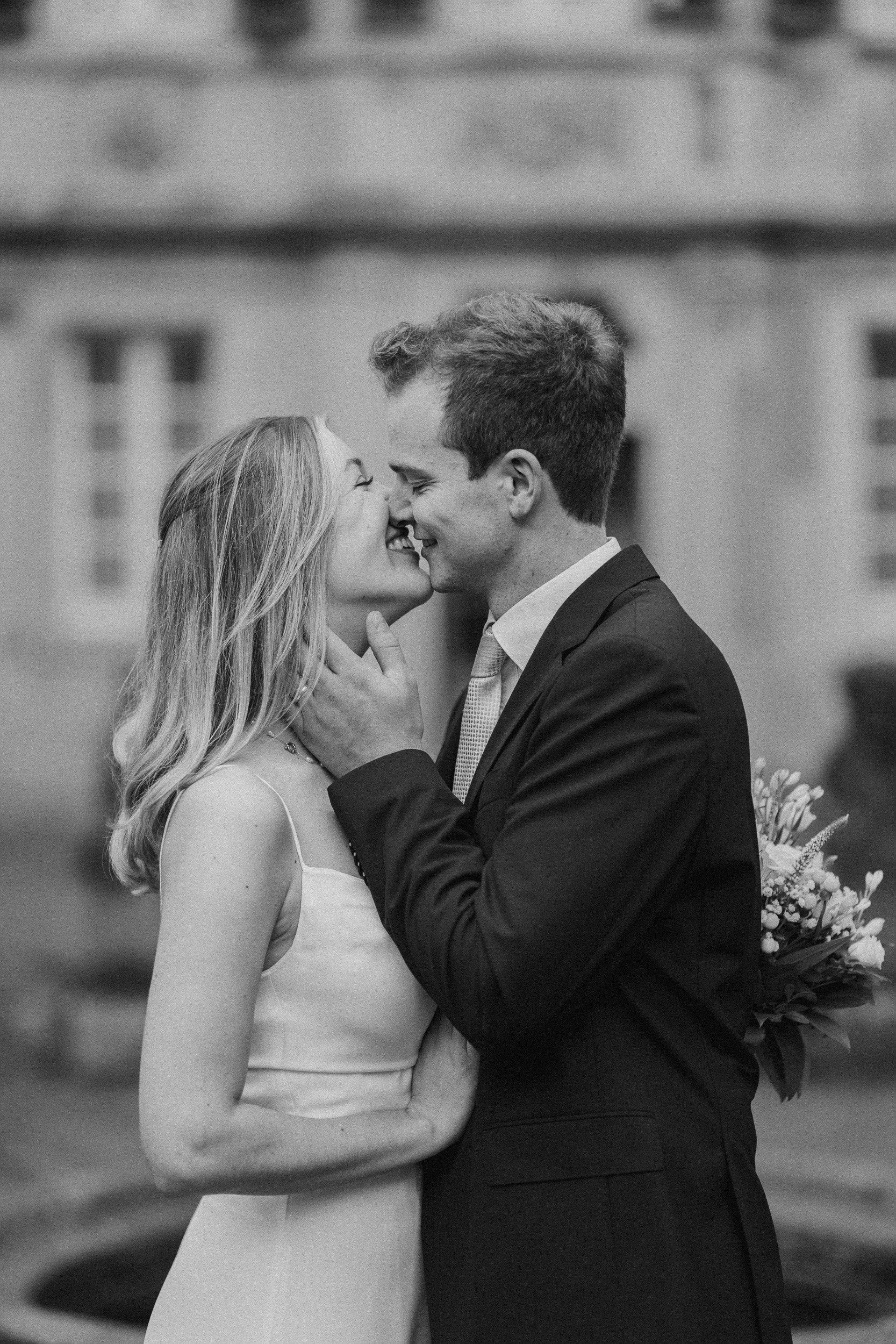 Ein Mann und eine Frau, die sich liebevoll umarmen und küssen, bei einer Hochzeitszeremonie im Freien, Schwarz-Weiß-Foto.