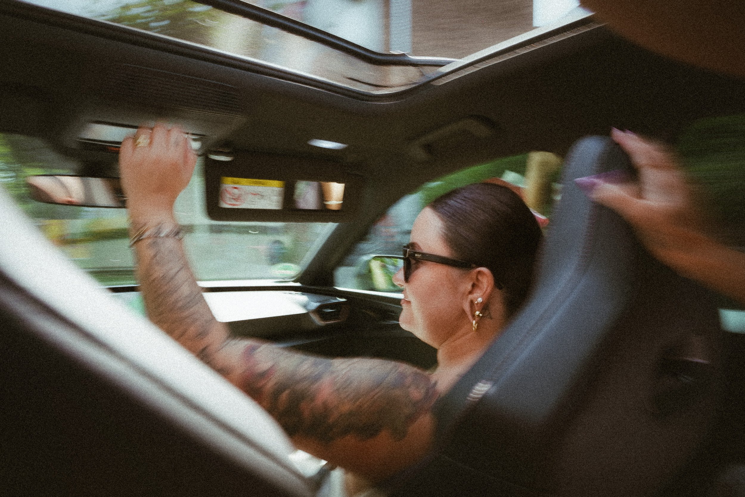 Eine Frau mit dunklen Haaren, Sonnenbrille, in einem Auto, die die Sonnenblende zurechtrückt.