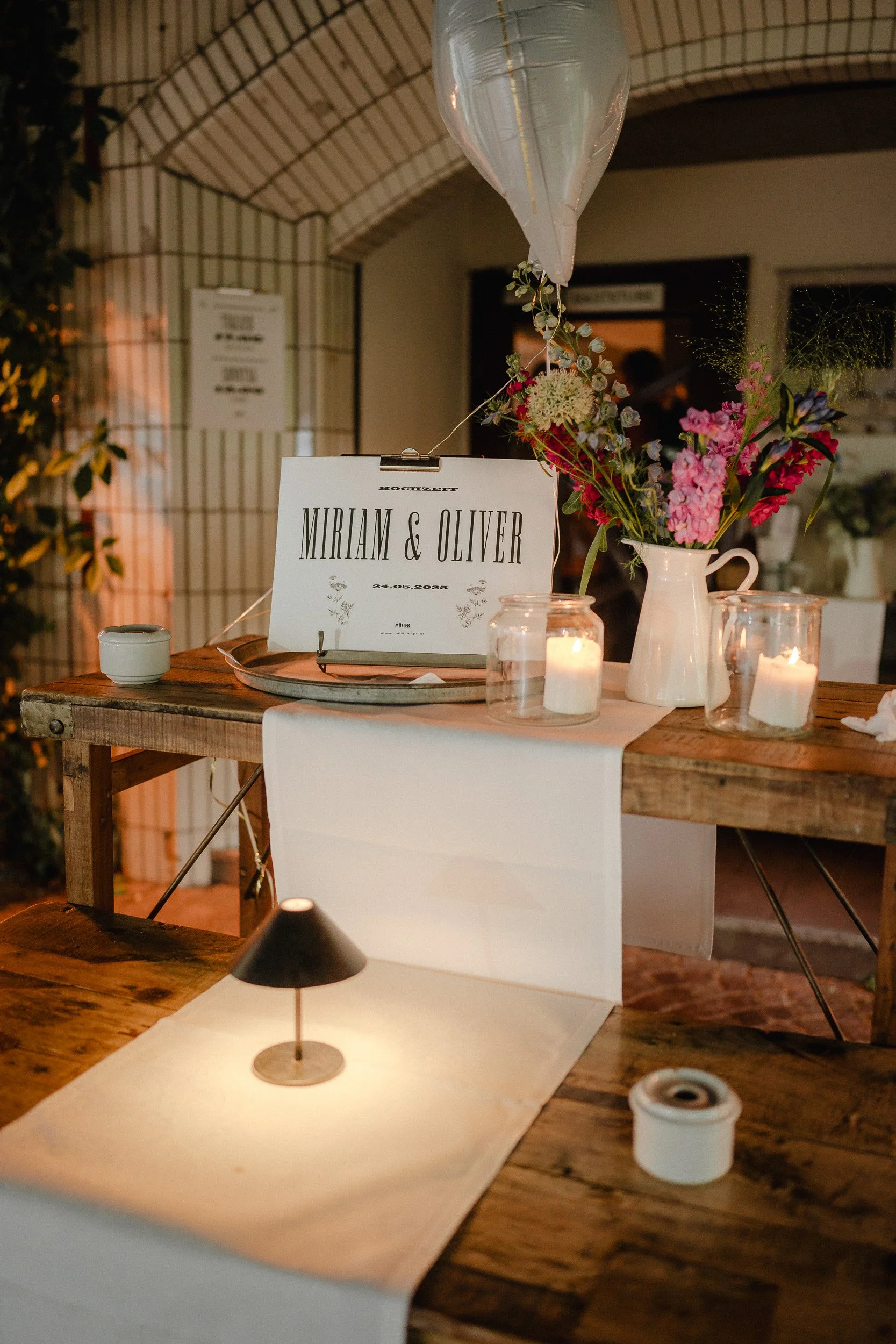 Tischdekoration für eine Hochzeit mit Blumen, Kerzen und einem Name-Schild 'Miriam & Oliver', Datum 24.05.2020, im rustikalen Stil.