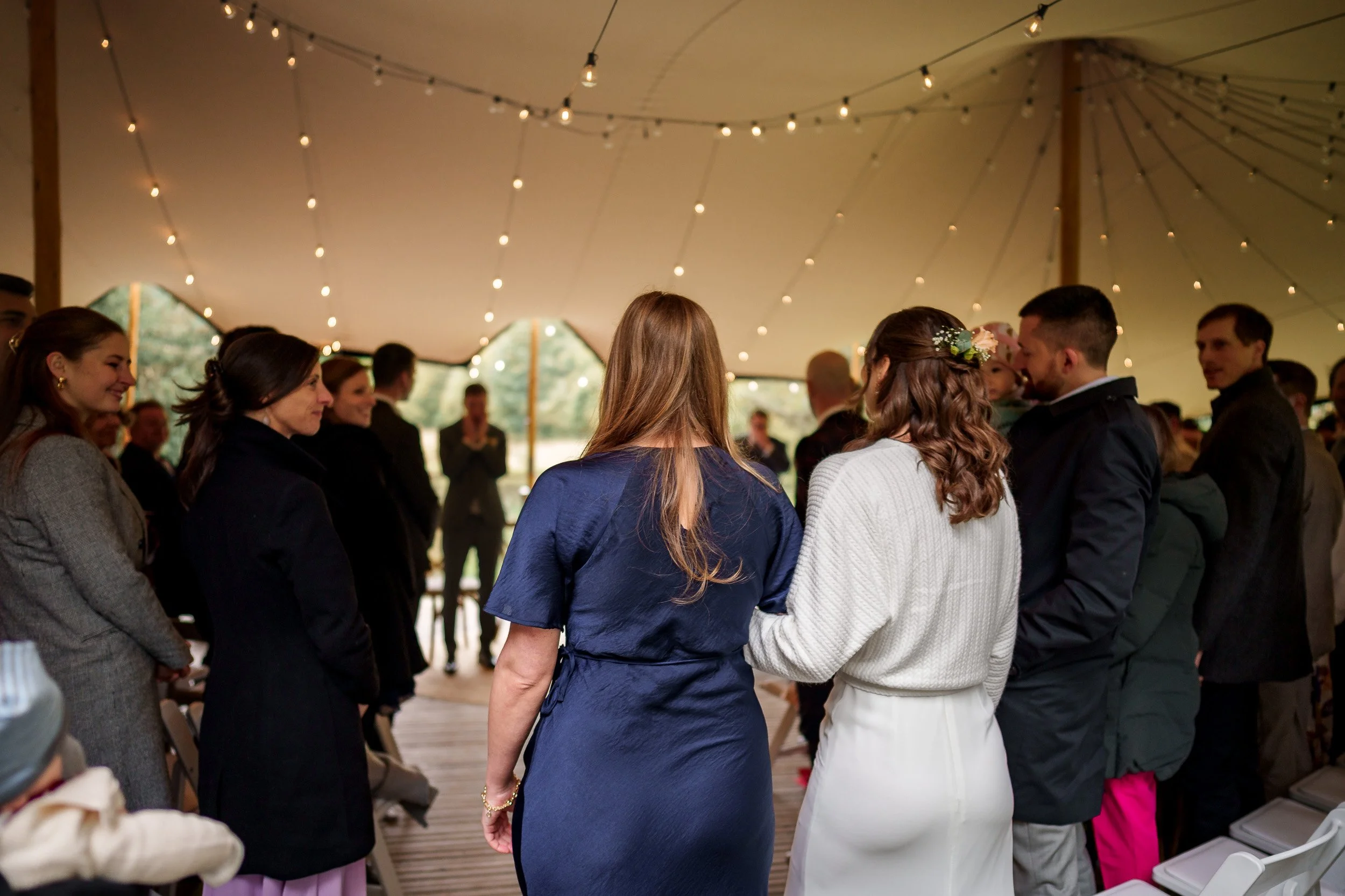 Menschen bei einer Hochzeitszeremonie im Zelt, die sich die Hände halten, unter warmem Lichterhimmel.