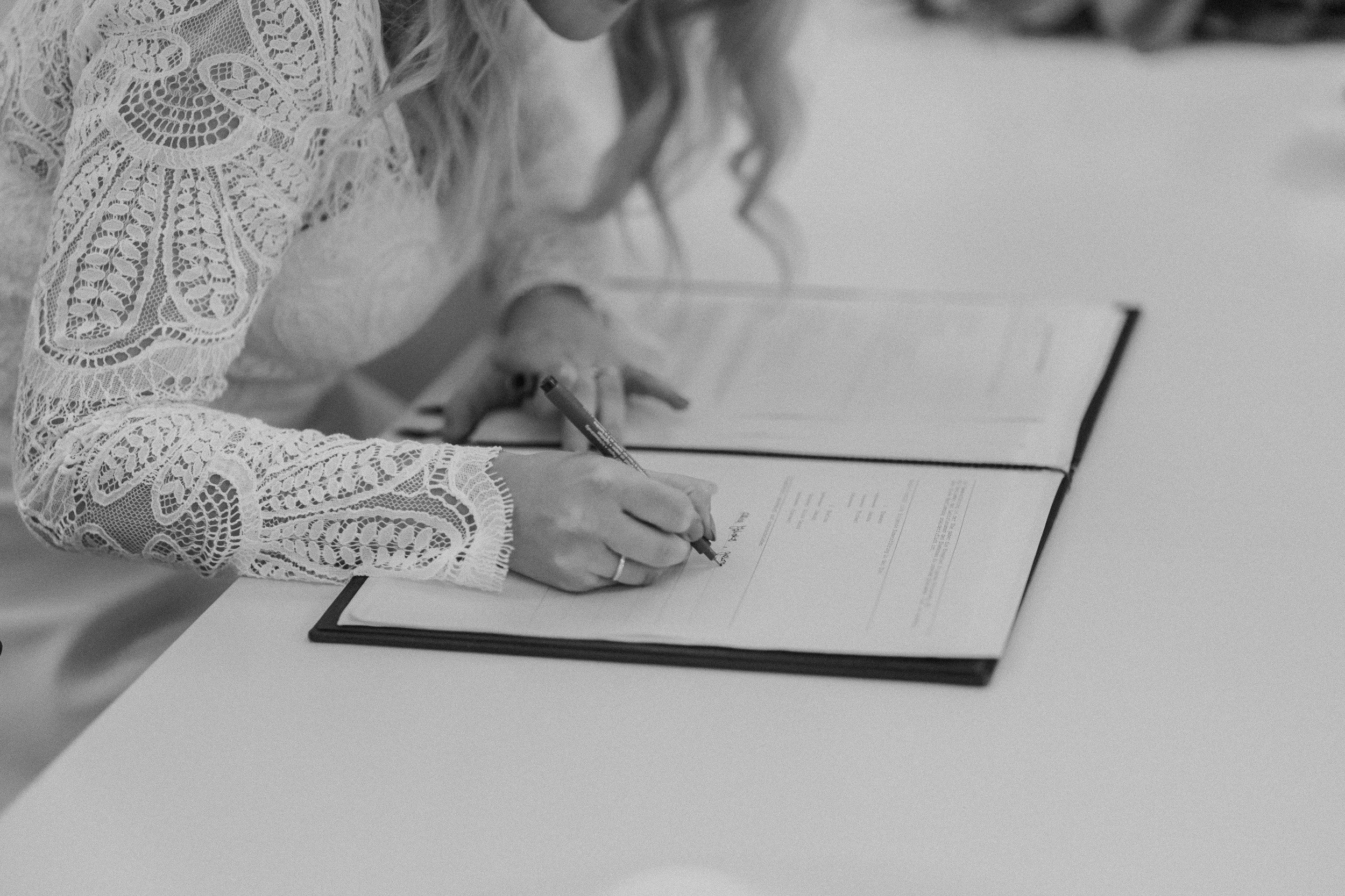 Frau schreibt auf einem Dokument mit einem Füllfederhalter, trägt eine lace Bluse, auf einem weißen Tisch.