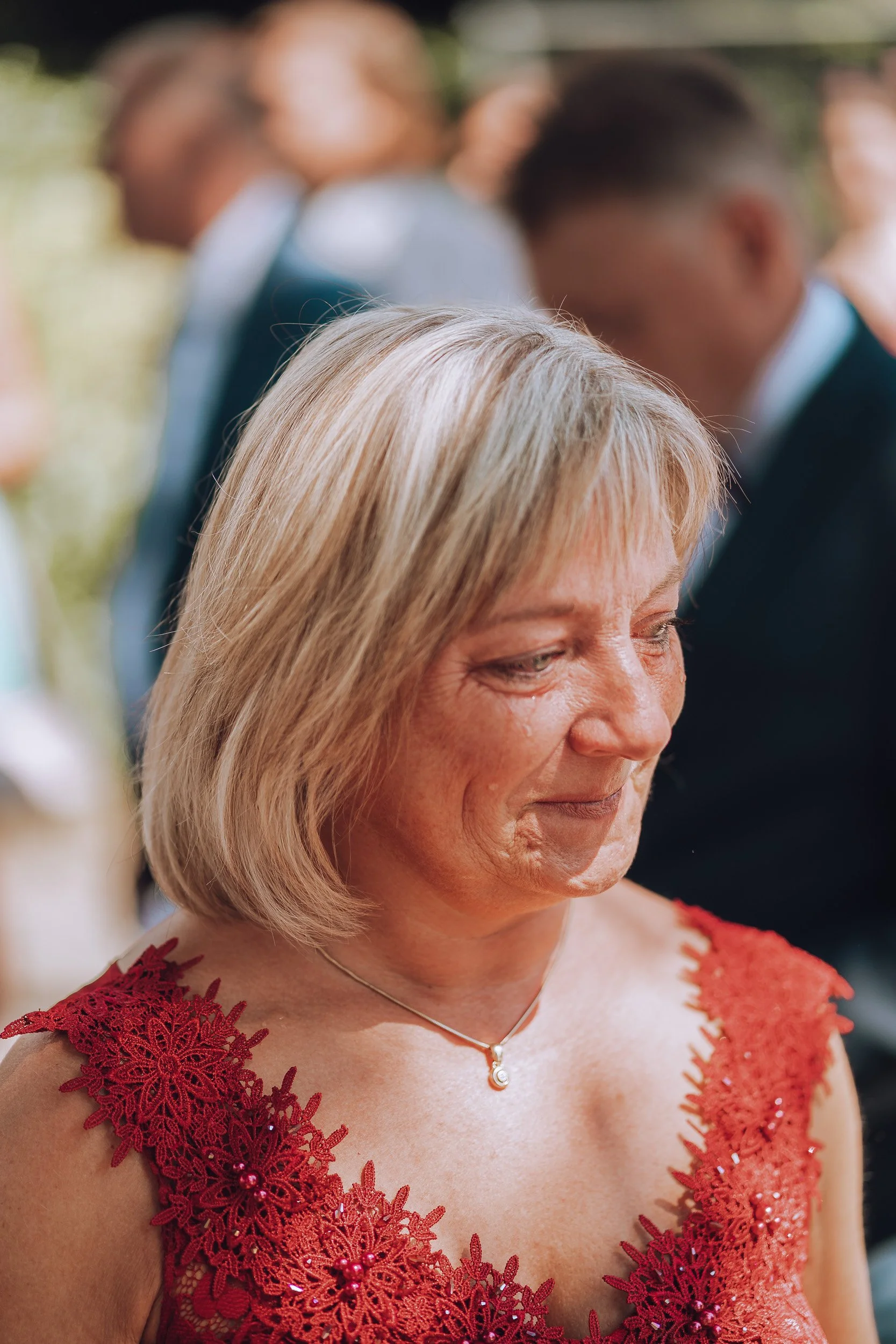 Nahaufnahme einer lachenden älteren Frau mit blonden Haaren in einem roten Kleid bei einer Feier im Freien.