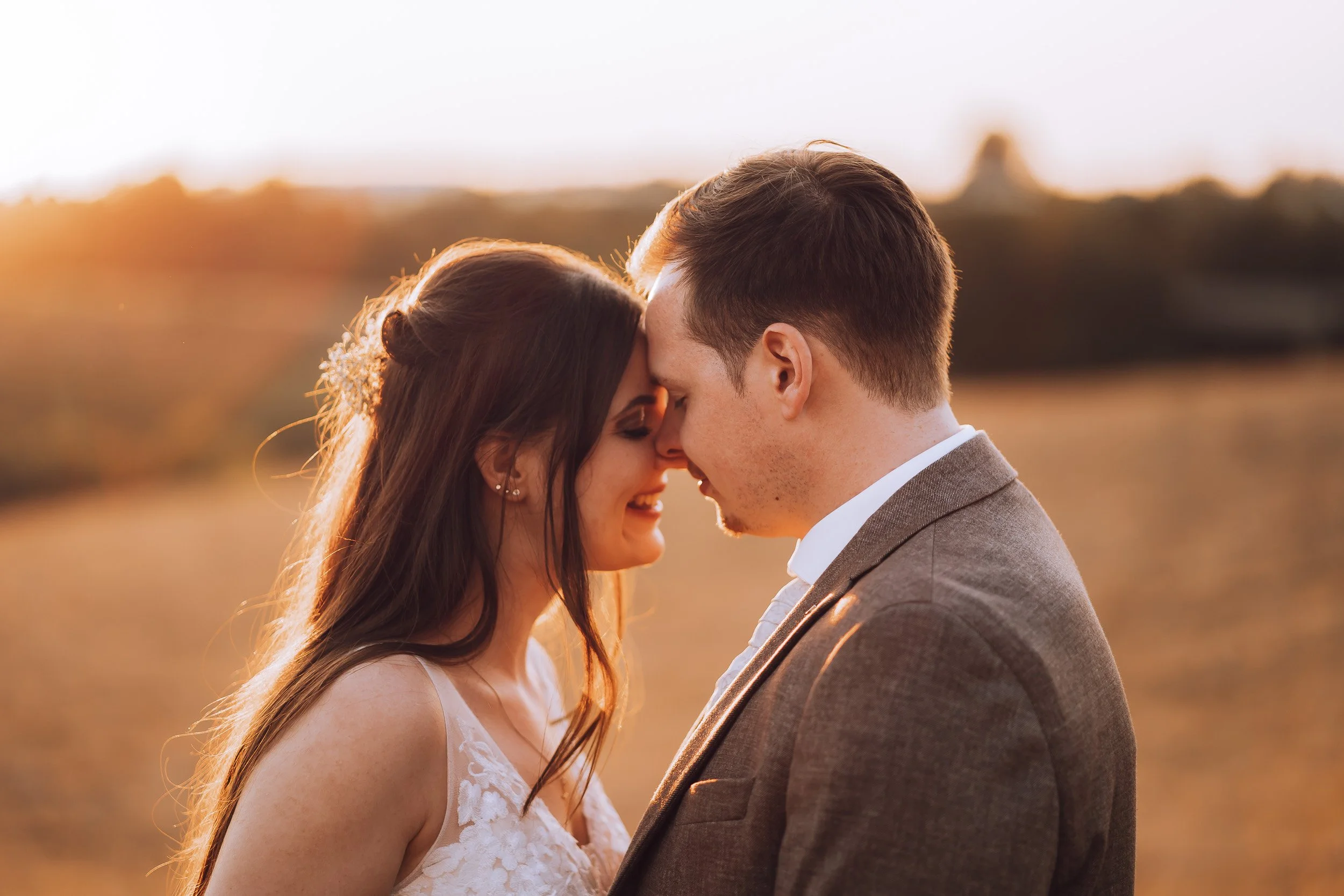 Ein Paar steht mit Stirn an Stirn in einem Sonnenuntergangsfeld, verliebt.