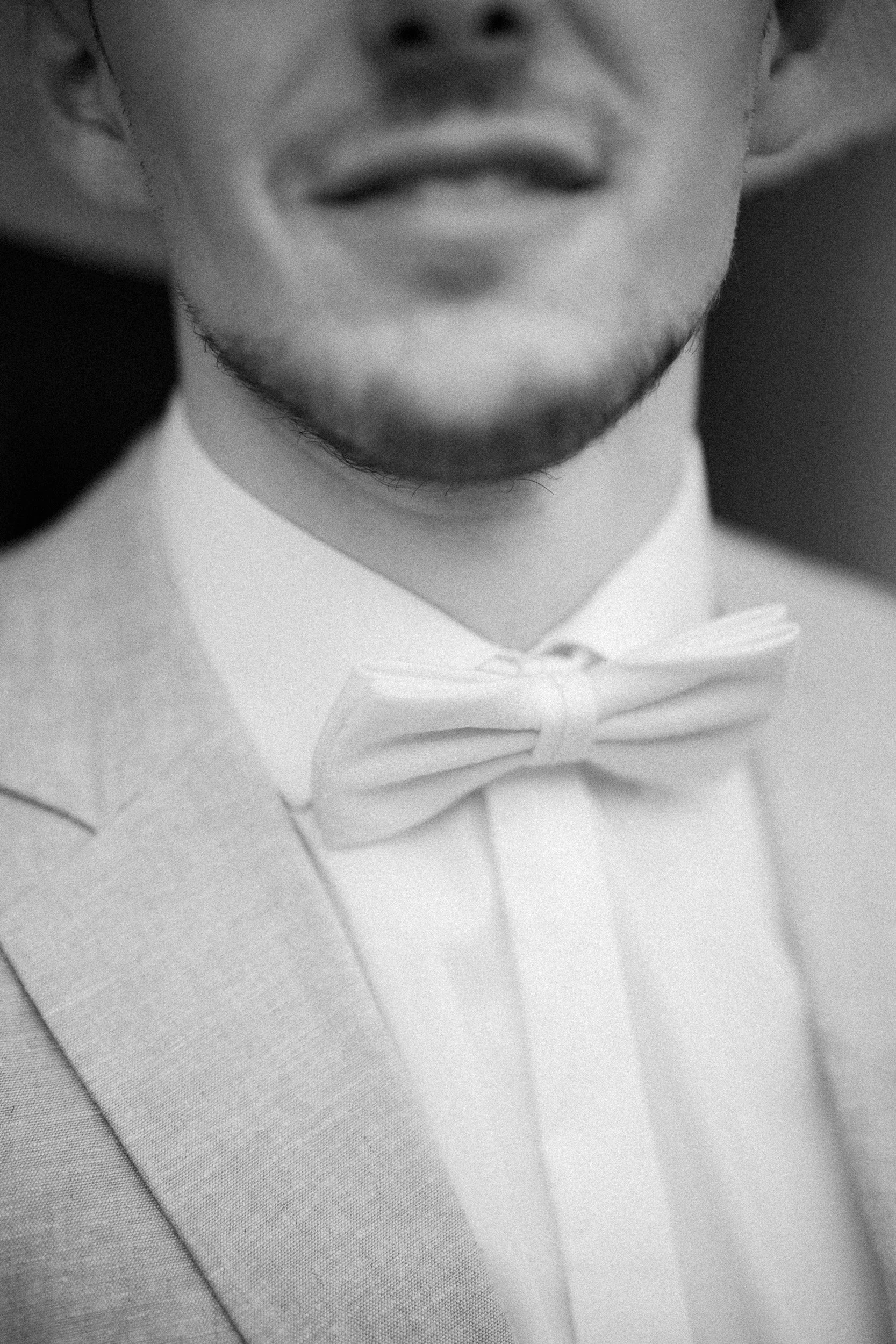 Nahaufnahme eines Mannes in formeller Kleidung mit Fliege, nur Mund und Kinn sichtbar, Schwarz-Weiß-Foto.