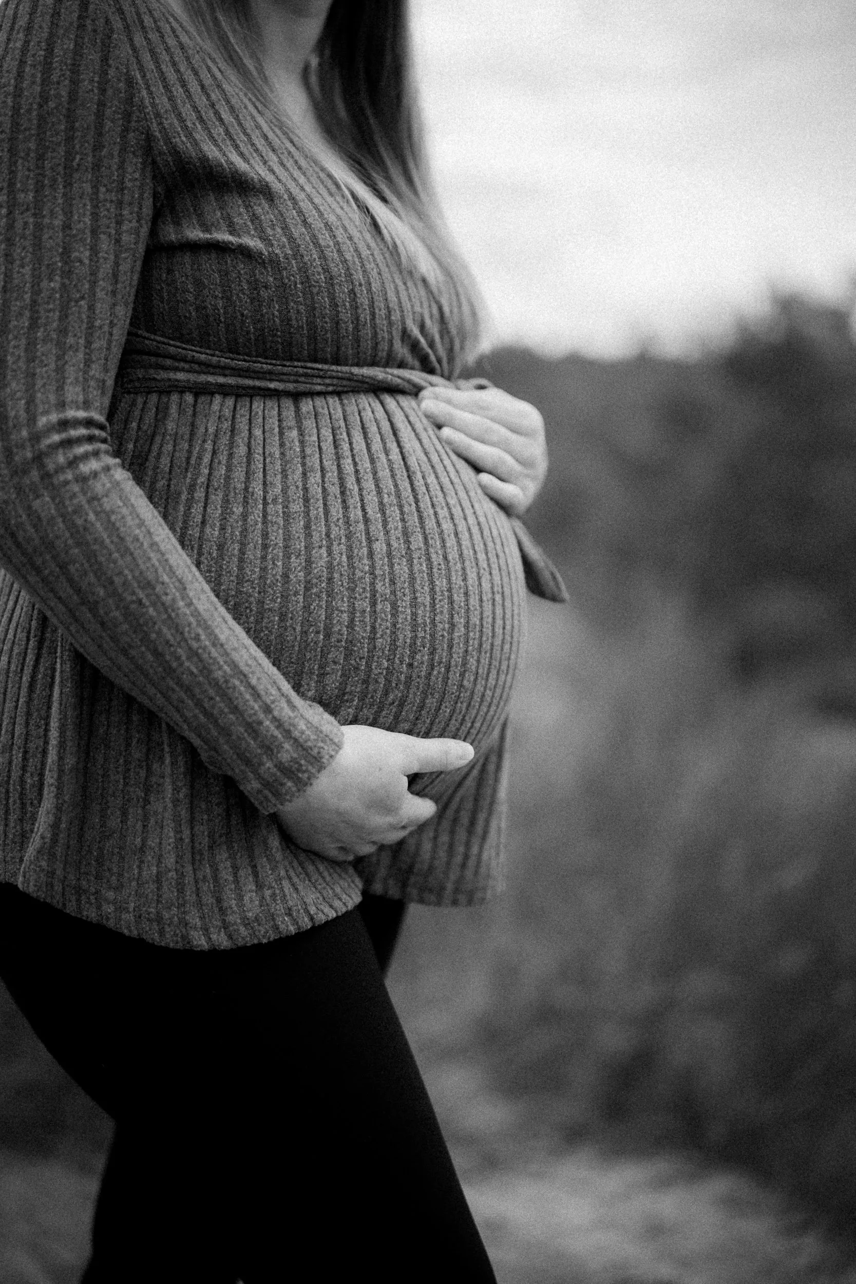 Schwangere Frau in einem langen Ärmel Pullover hält ihre Hände auf den Bauch, Schwarz-Weiß-Foto, outdoor.
