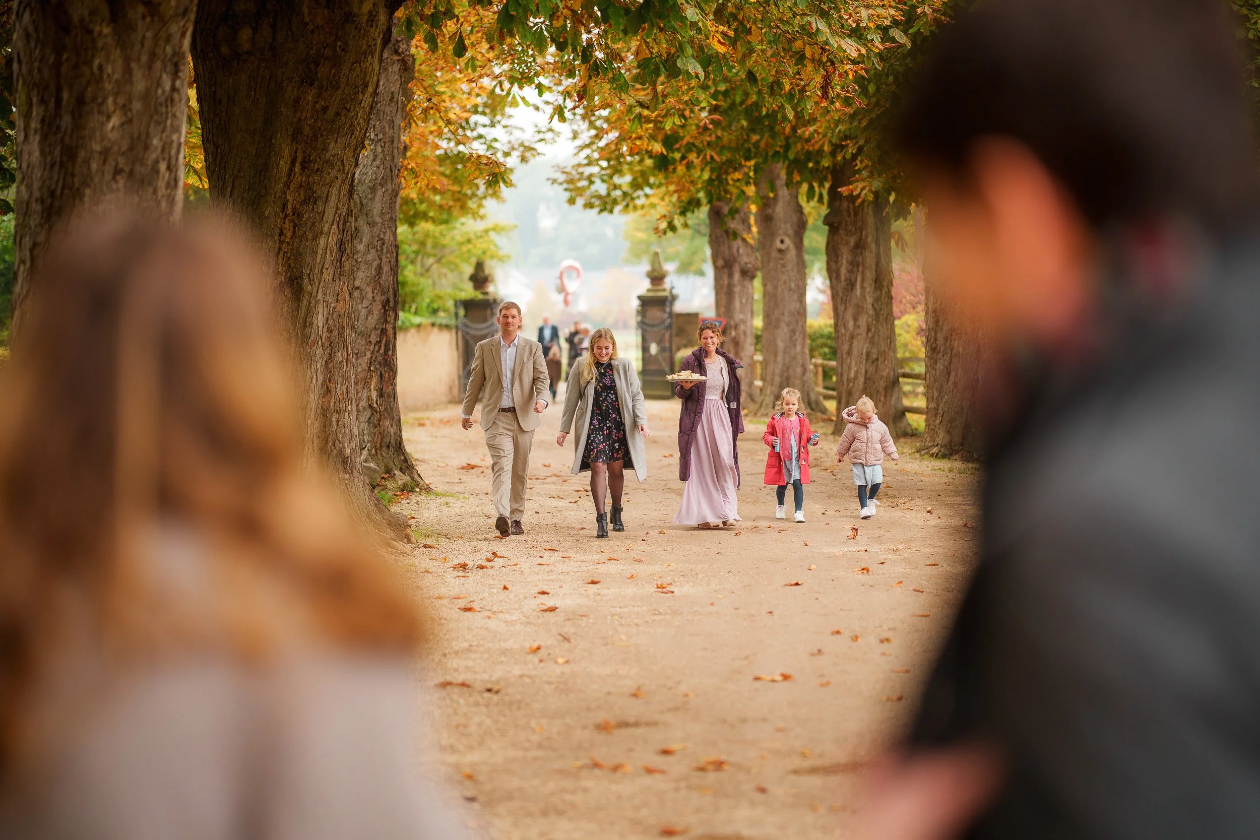 Familie spaziert im Park, Sicht durch Zweibein auf Spazierende, im Hintergrund Bäume mit Herbstlaub.