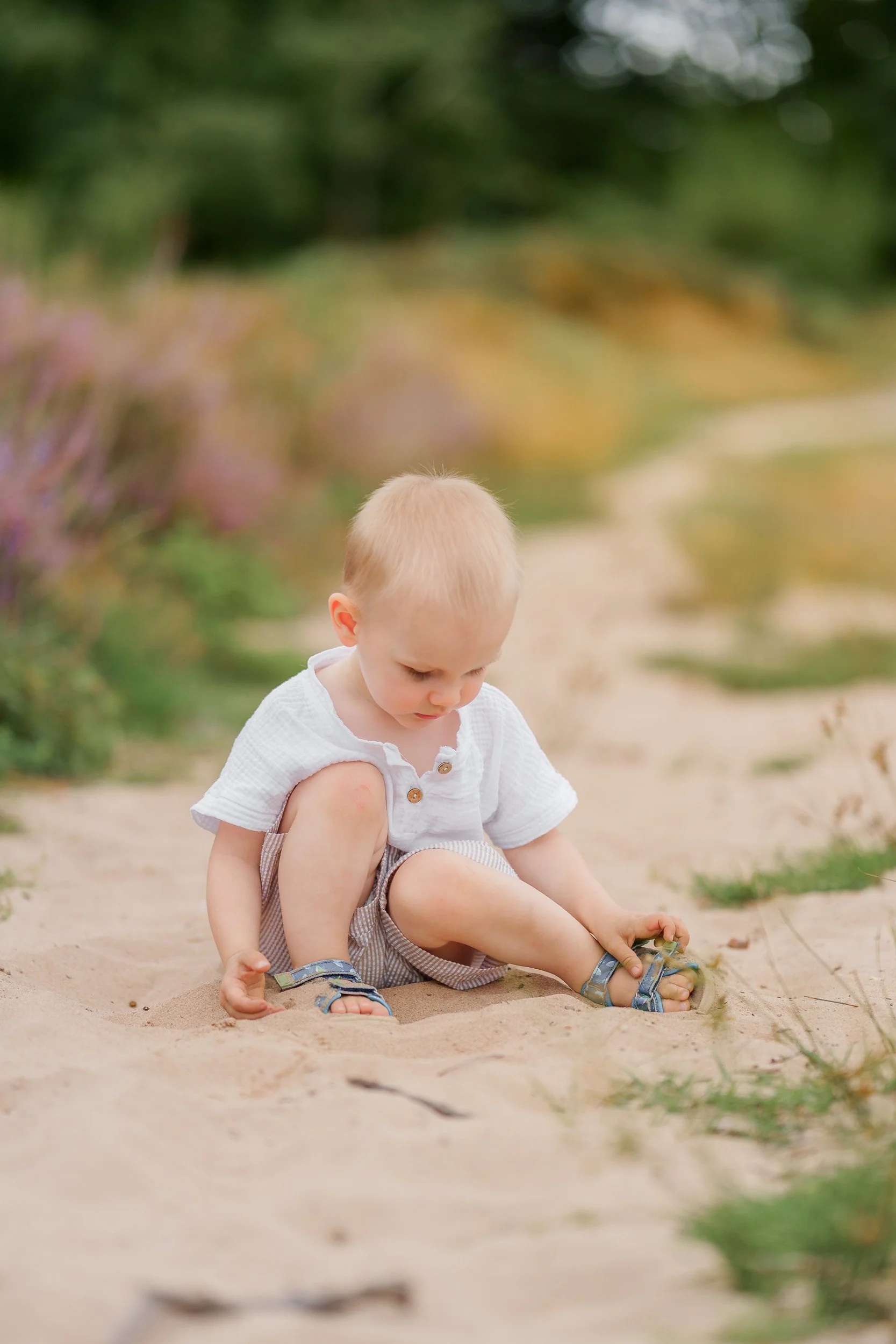 Ein kleiner Junge sitzt barfuß im Sand in einem Park und spielt mit dem Sand.