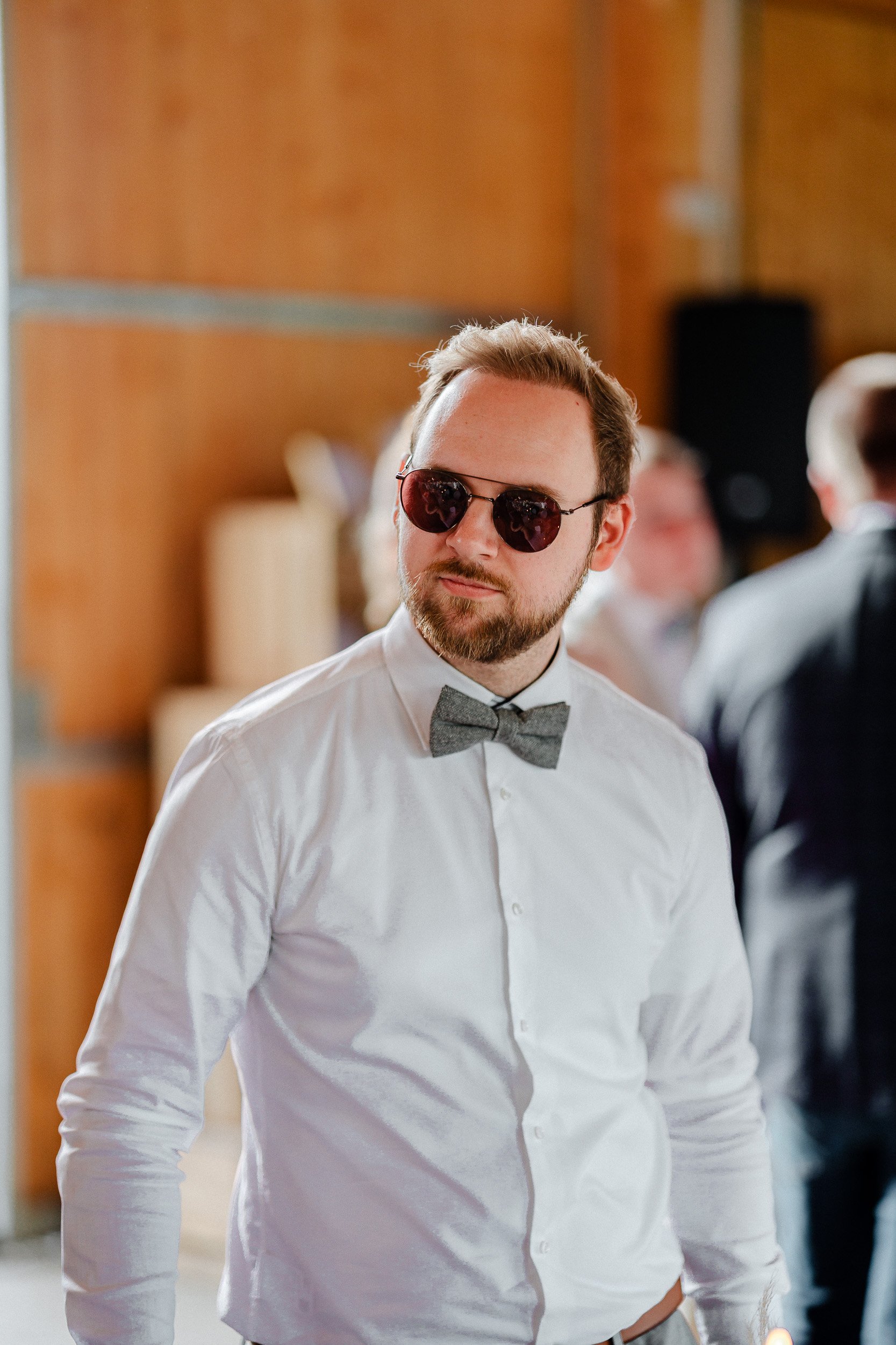 Mann in weißem Hemd, grauem Fliegen und dunkelroten Sonnenbrillen auf einer Party