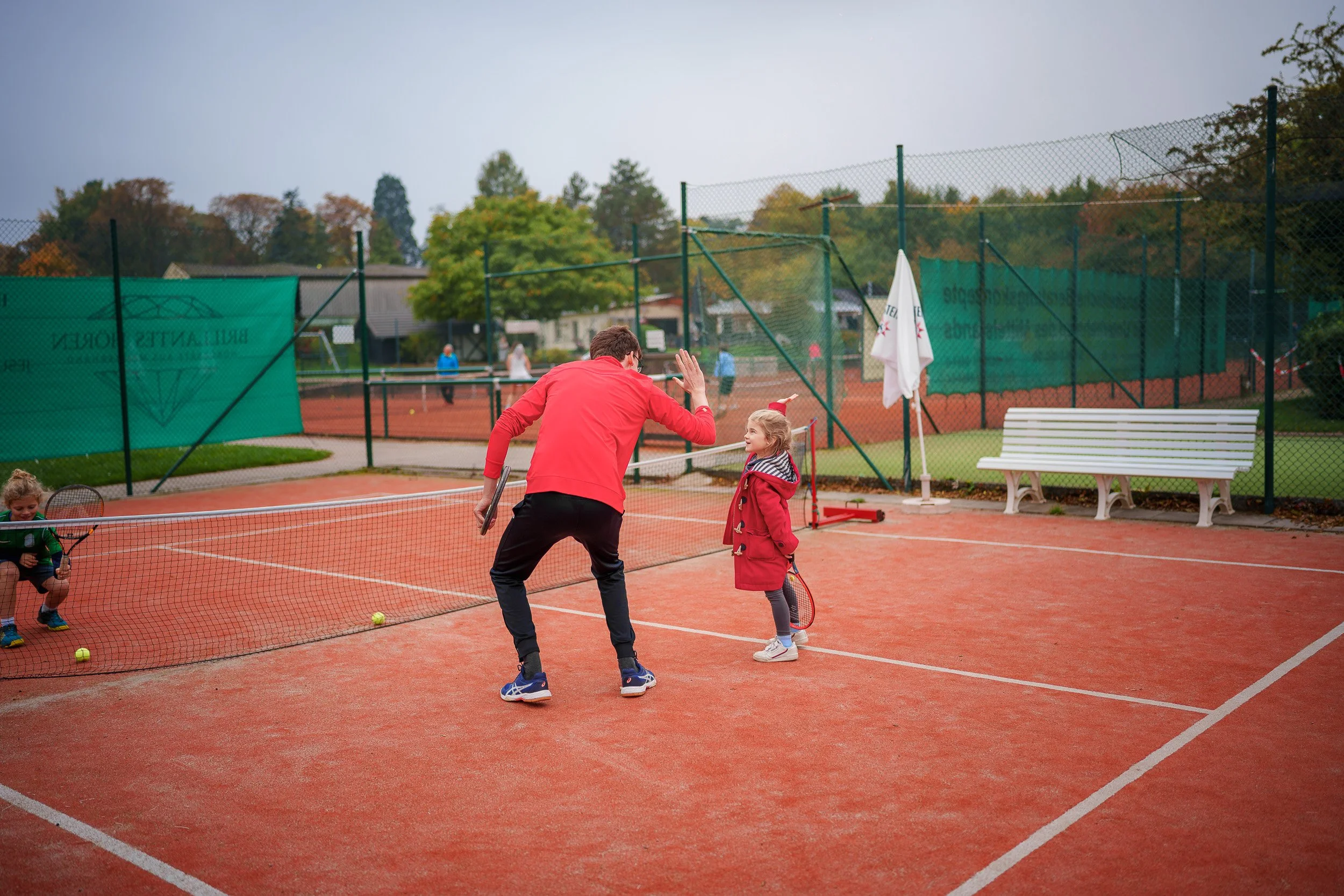 Ein Tennislehrer gibt einem jungen Mädchen auf der Tennisanlage Tipps und ein High-Five, während sie Tennis spielen.