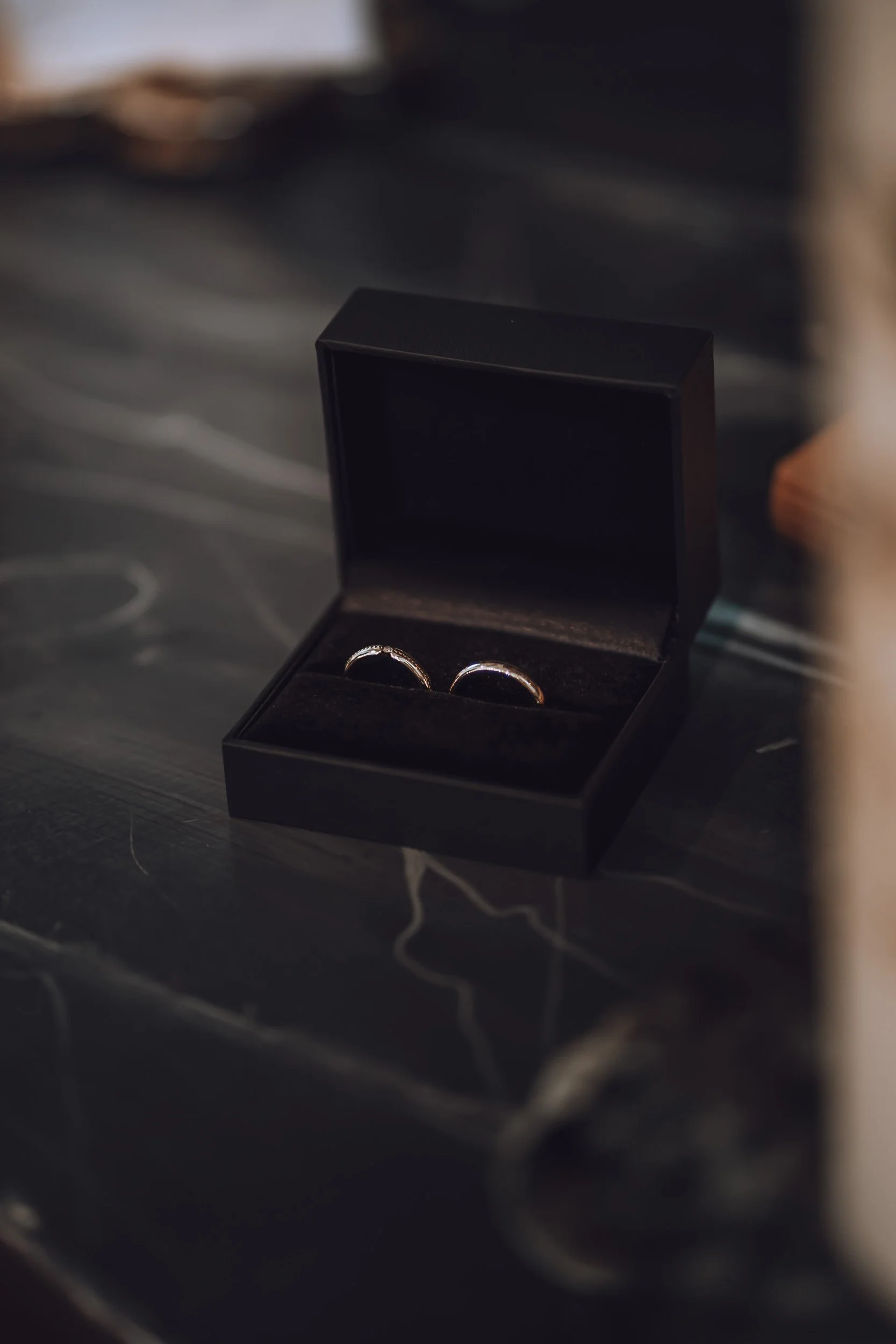 Schwarze Schmuckschatulle mit zwei Eheringen auf schwarzem Marmor.