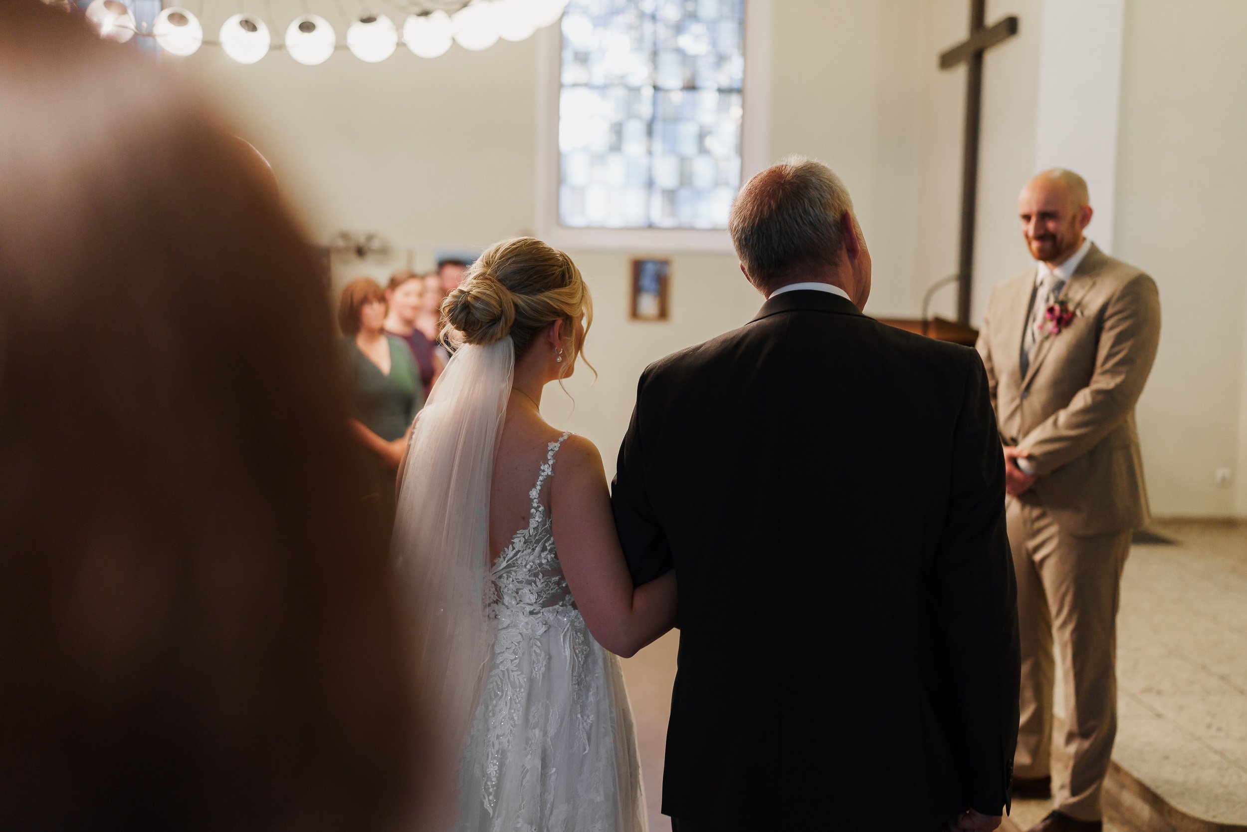 Hochzeit im Kirchenraum mit Braut, Vater und Bräutigam, während das Paar das Ja-Wort gibt.