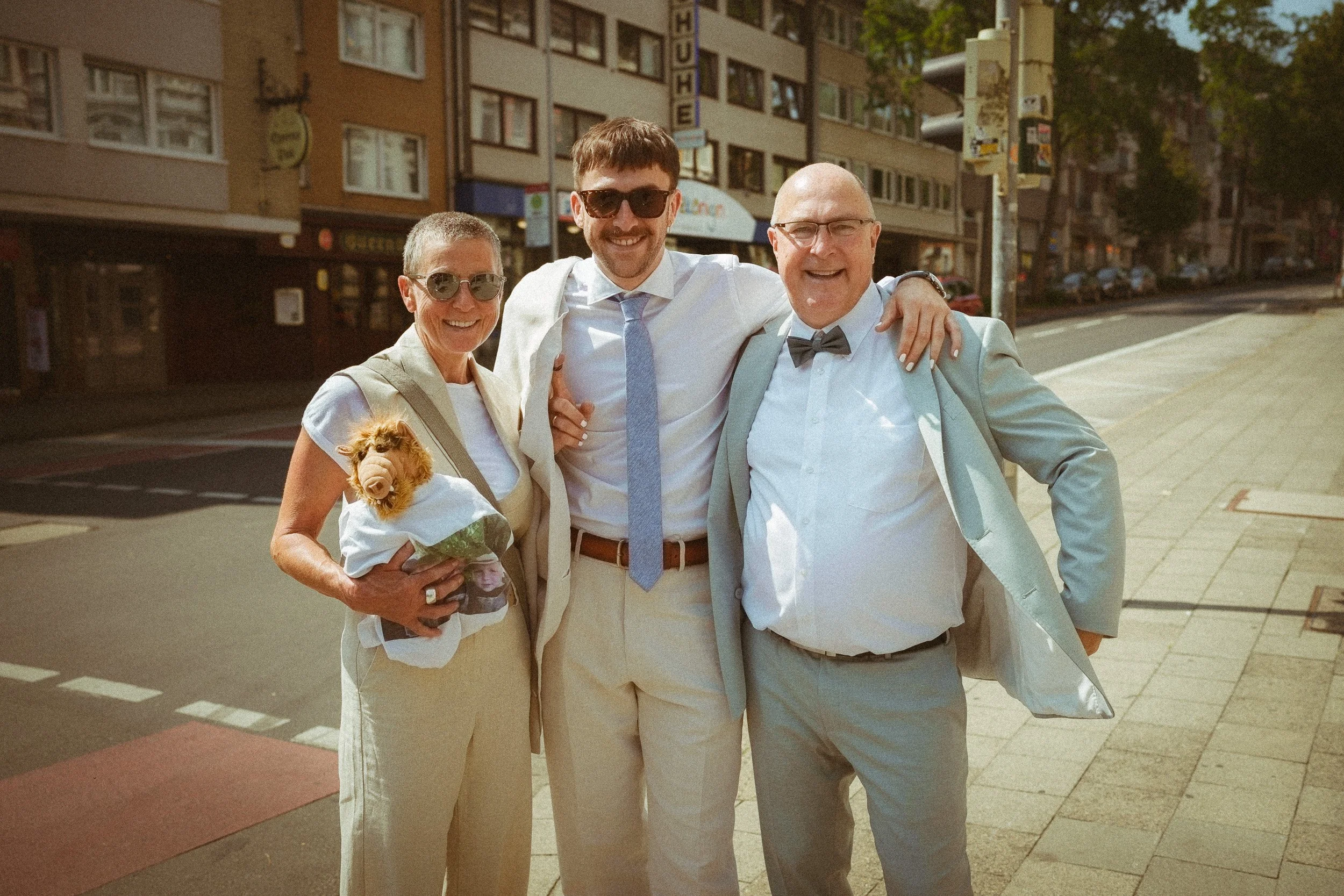 Vier Menschen stehen zusammen auf einer Stadtstraße, lachen und umarmen sich, eine Person hält einen kleinen Hund in den Armen.