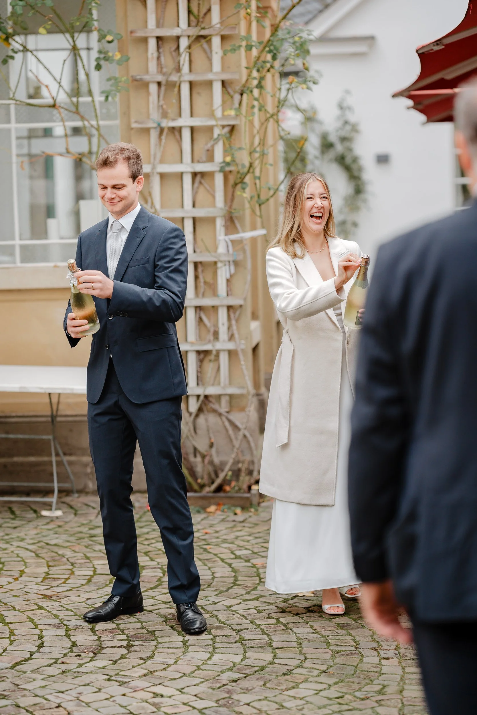 Menschen bei einer Feier im Freien, die Sektflaschen halten, lachen und sprechen.