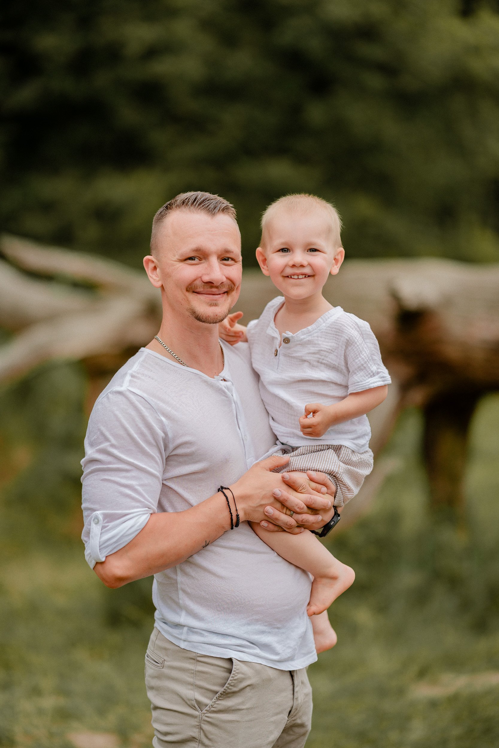 Ein Mann hält ein lachendes kleines Kind bei Sonnenuntergang im Freien, umgeben von Natur.