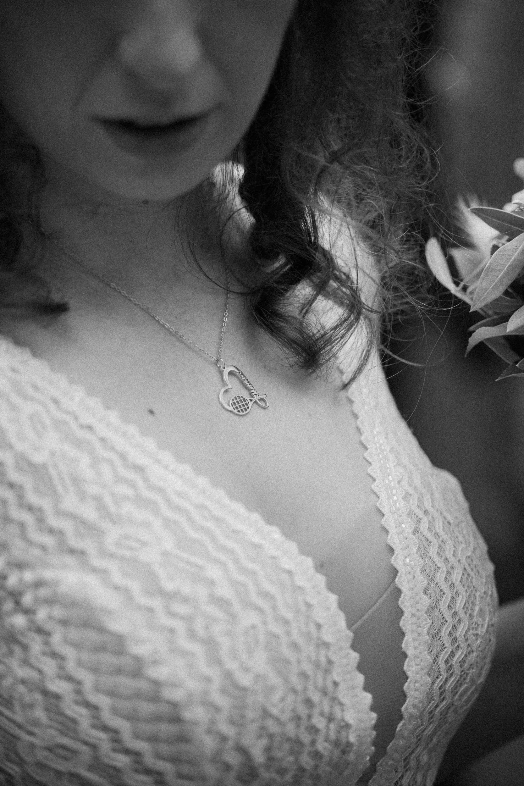 Nahaufnahme einer Frau mit lockigem Haar, die ein Herz-förmiges Schmuckstück trägt, während sie eine Blume hält.