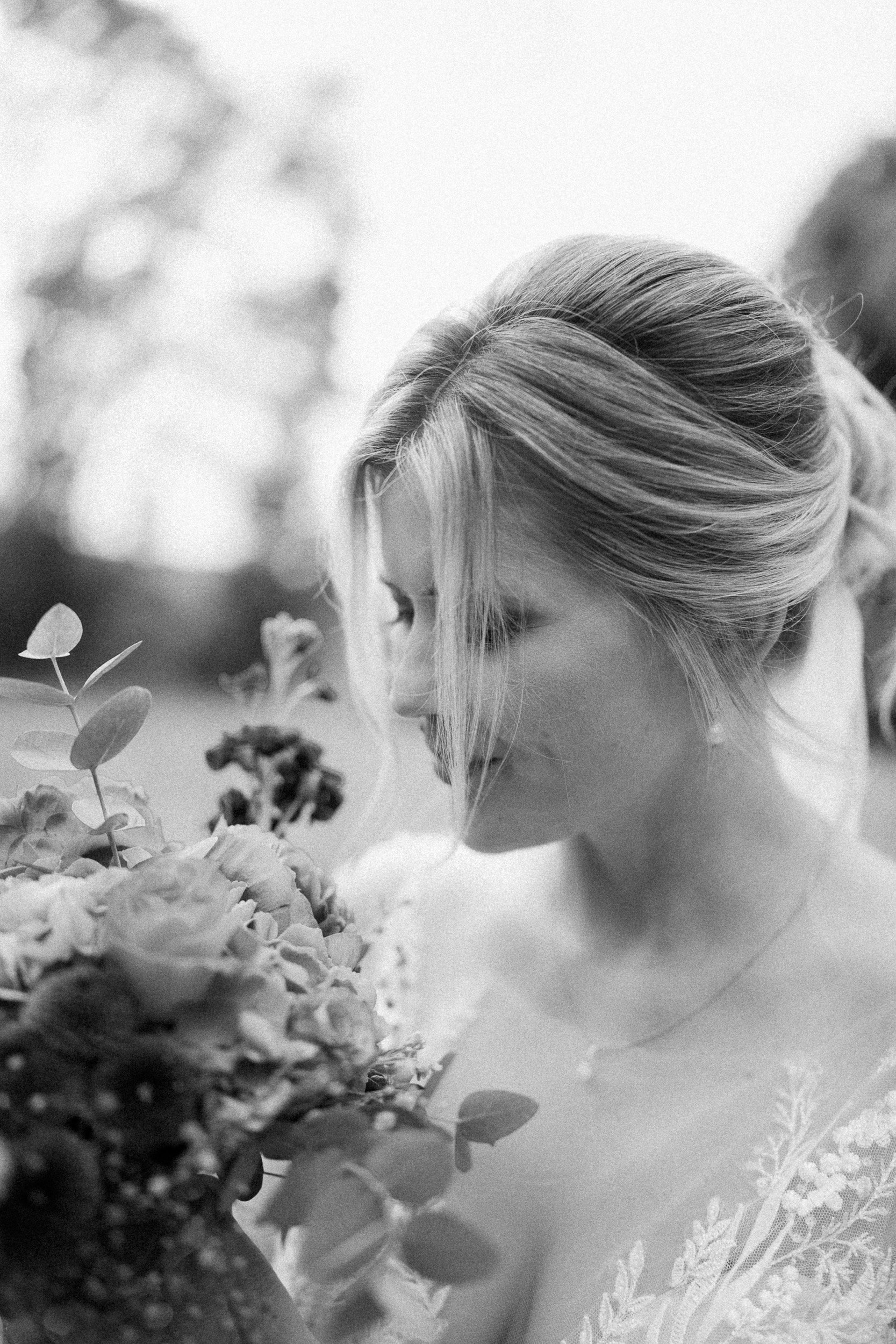 Schwarz-weiß-Foto einer glücklichen Frau, die ein Blumenbukett hält und liebevoll daran schnuppert, im Freien bei Sonnenuntergang.